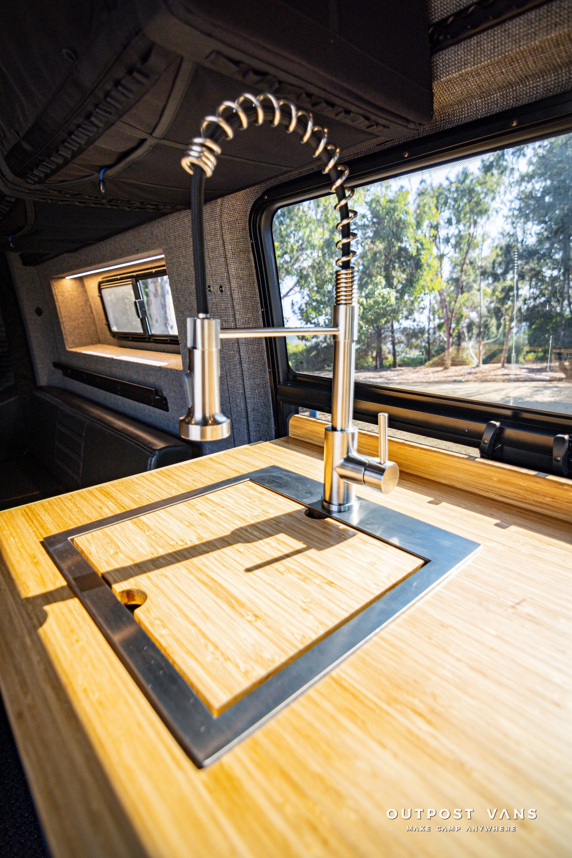 A kitchen sink is sitting on top of a wooden counter in a van.