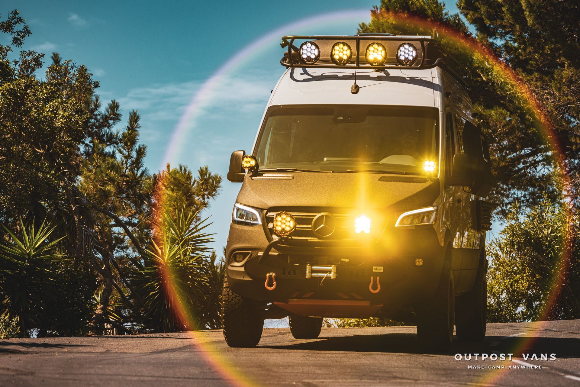 A van with a rainbow in the background is parked on the side of the road.