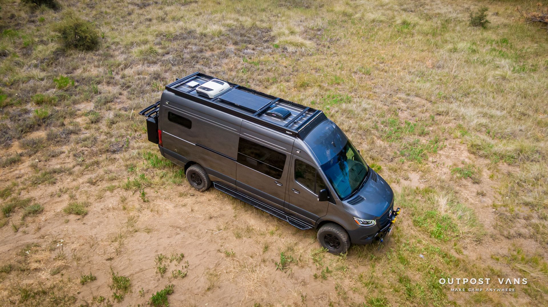 An aerial view of a black van parked in the middle of a dirt field. Outpost vans Sprinter 170 AWD.