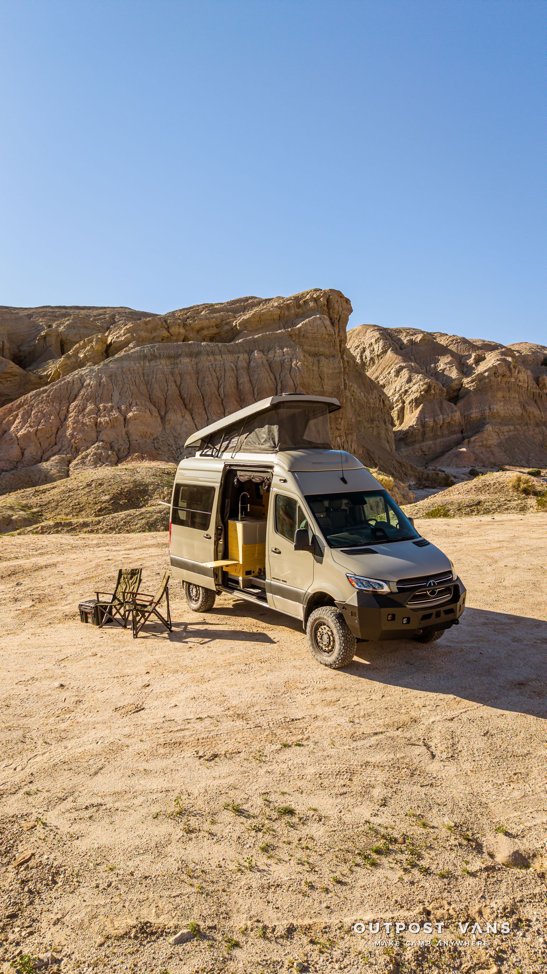 Small camper van parked in a rocky desert landscape under a clear blue sky.