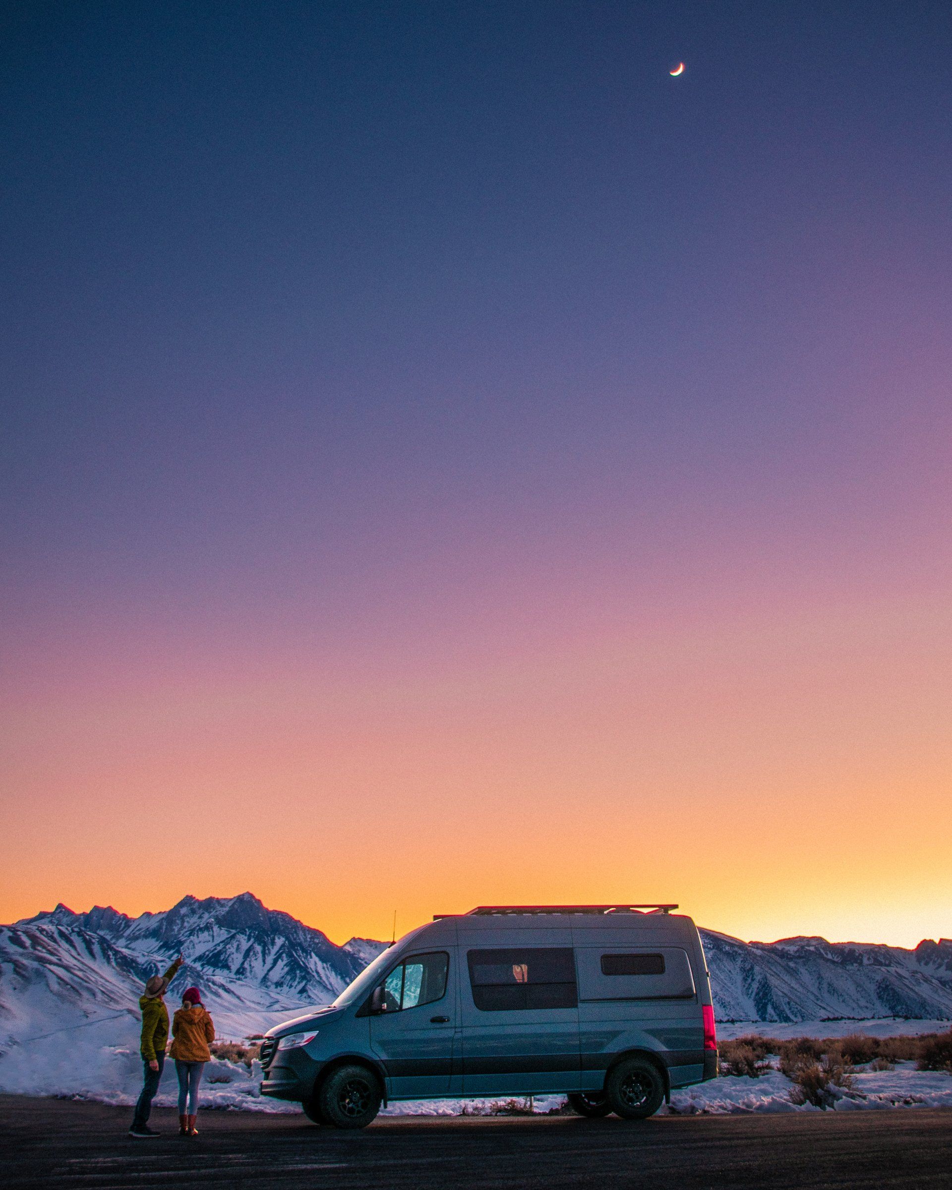 a couple of people are standing next to a van parked on the side of the road .