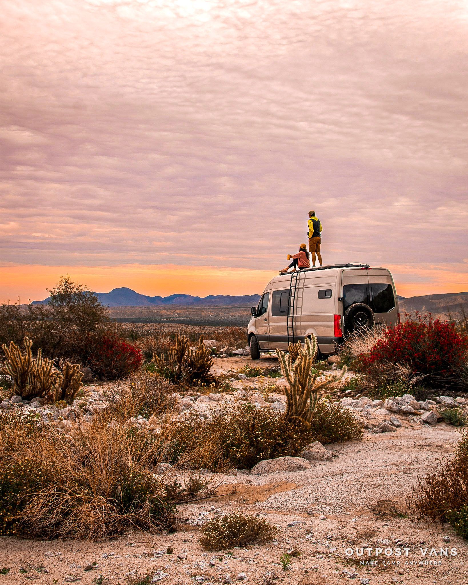 a couple of people standing on top of a van in the desert .