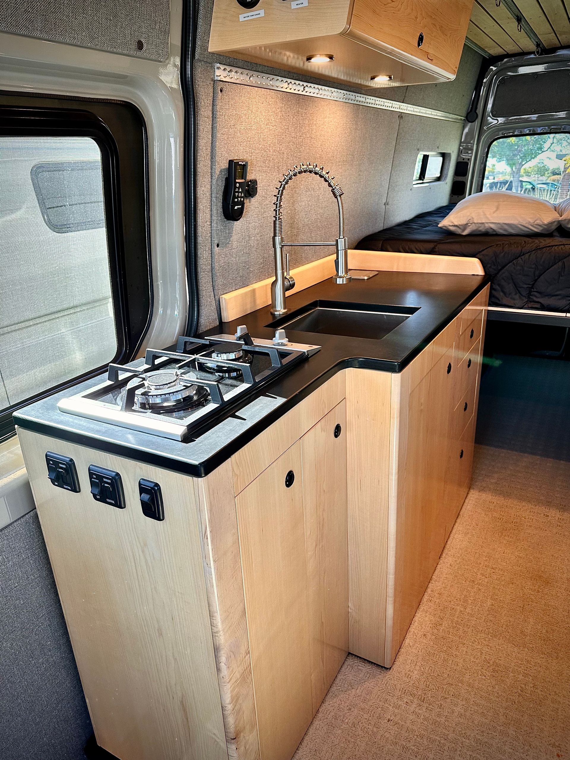 a kitchen in a van with a sink , stove and a bed .