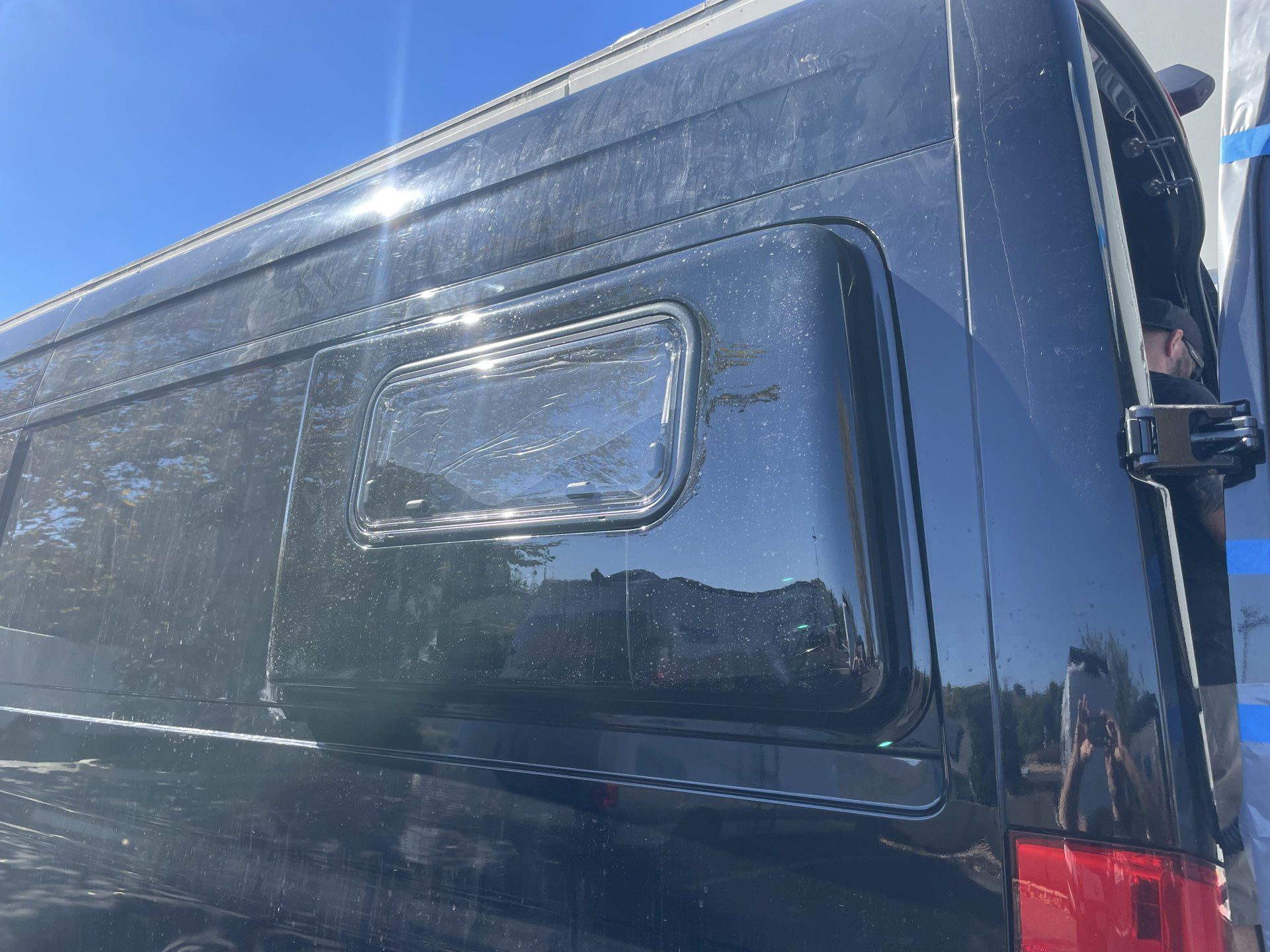 A black van with a window on the side is parked in a parking lot.
