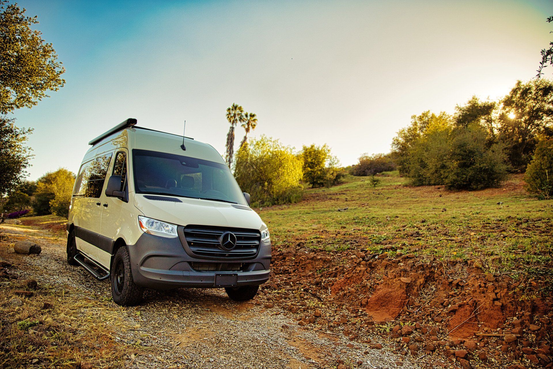 A white van is parked on the side of a dirt road in a field.