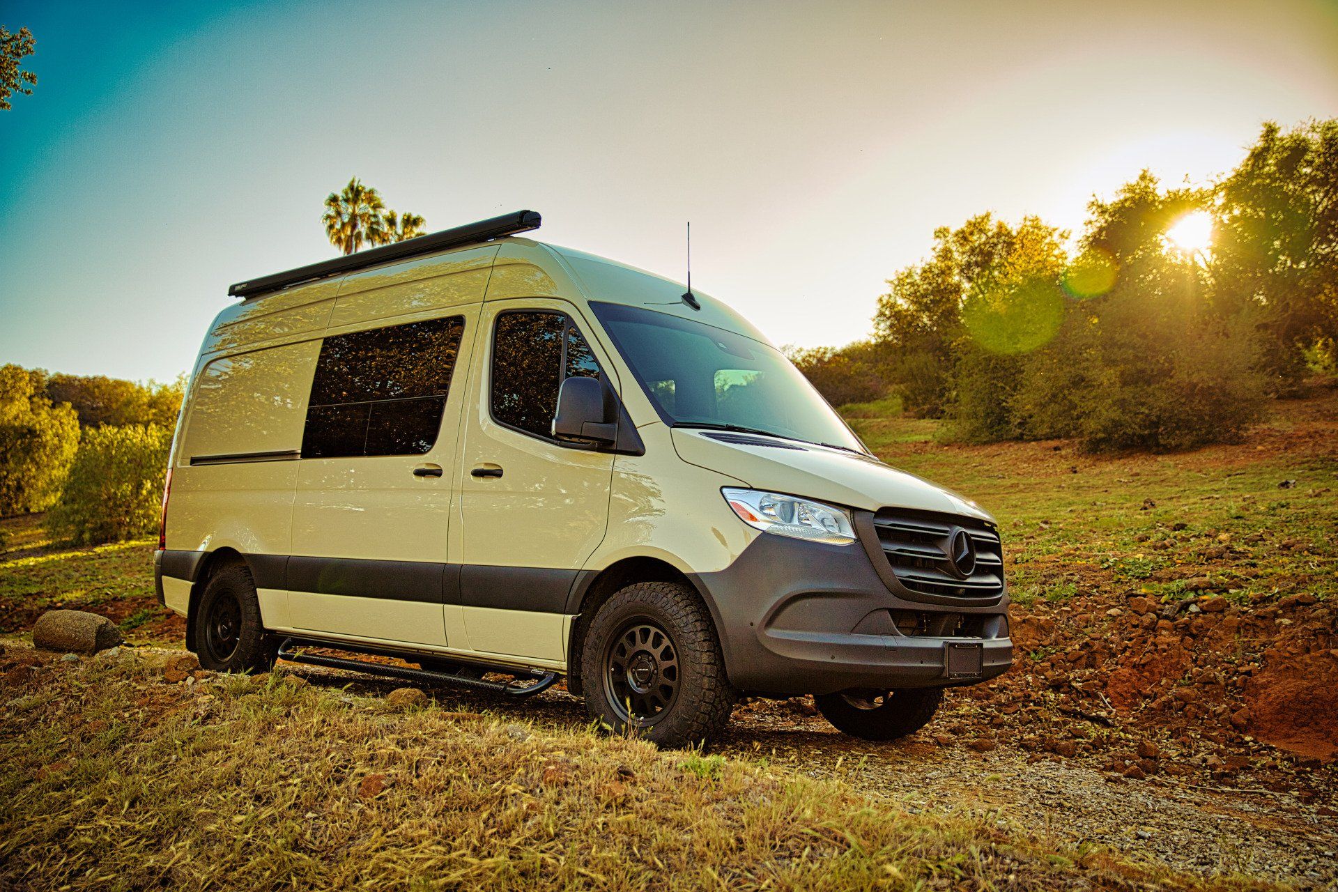 A white van is parked on the side of a dirt road in a field.
