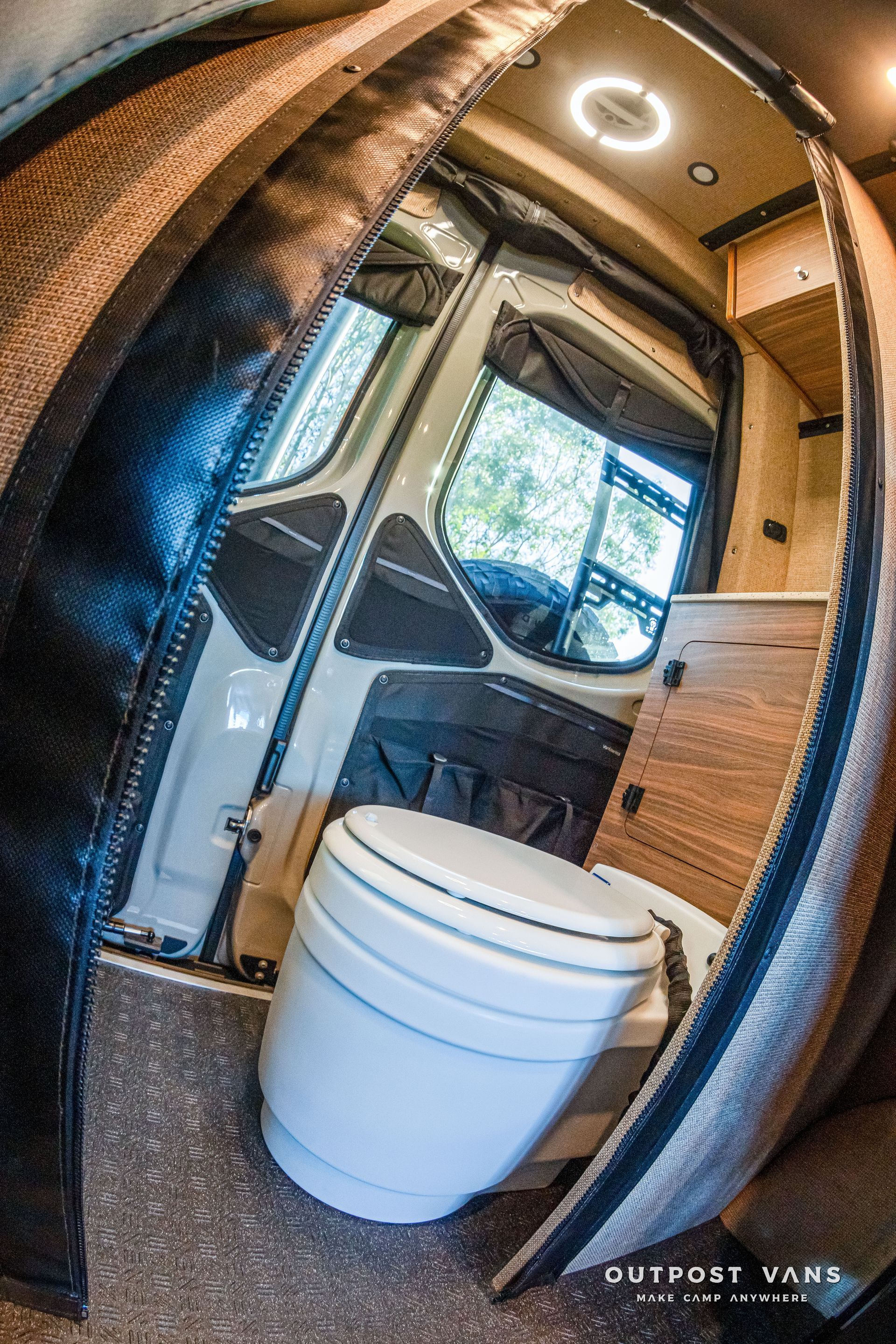 Inside a van: a toilet, windows, and wood accents. Brown and black walls.