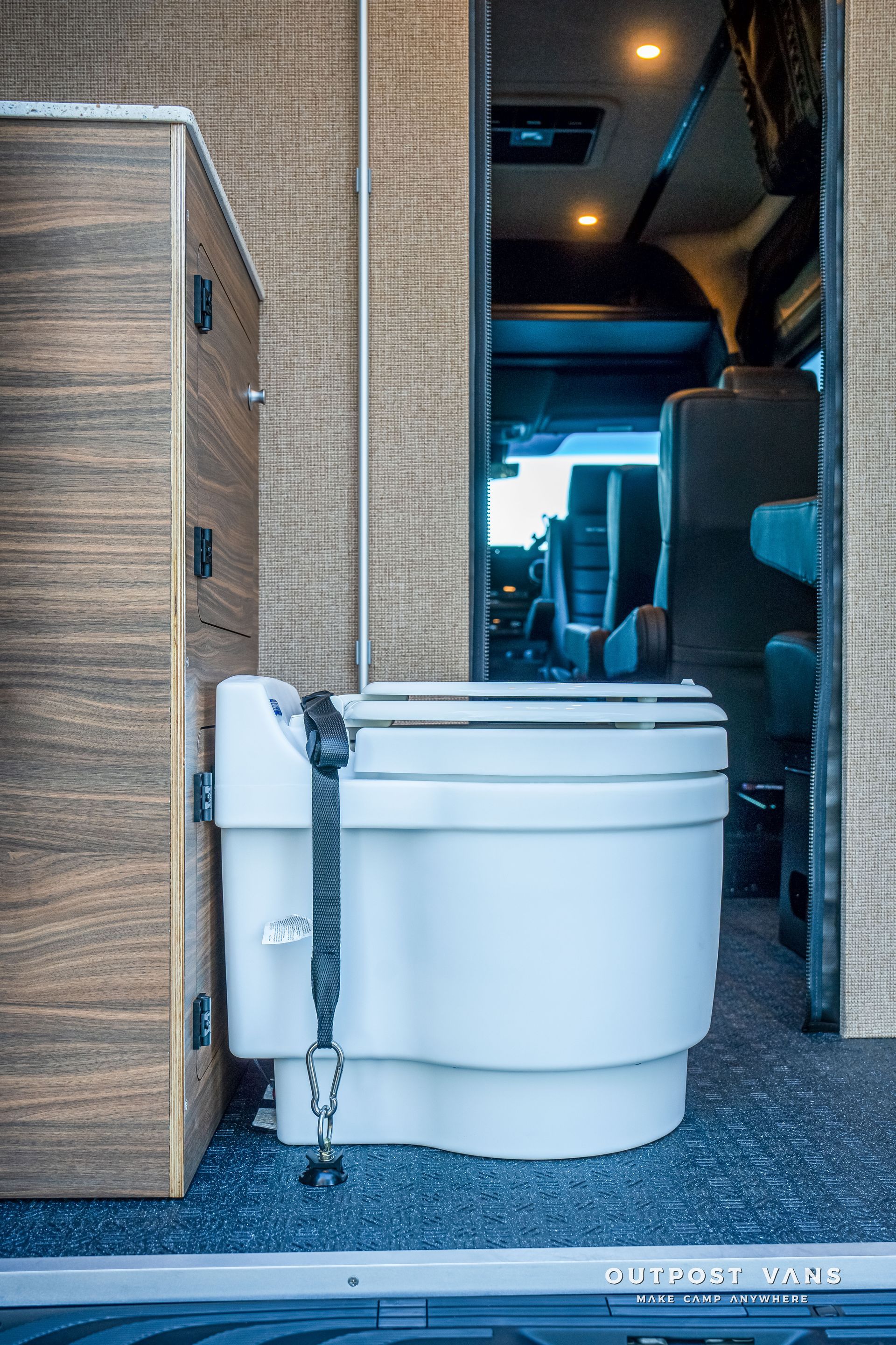 Toilet in a van interior with adjacent wooden cabinet.
