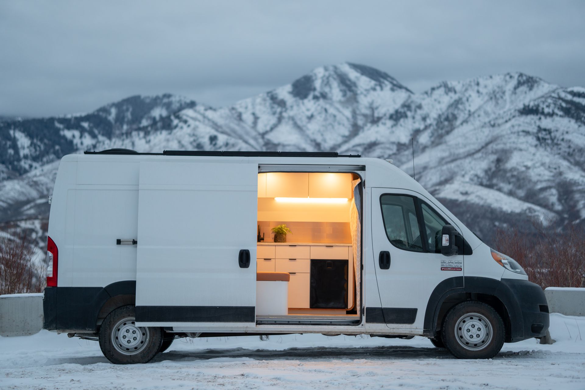 A white van is parked in the snow with its doors open.