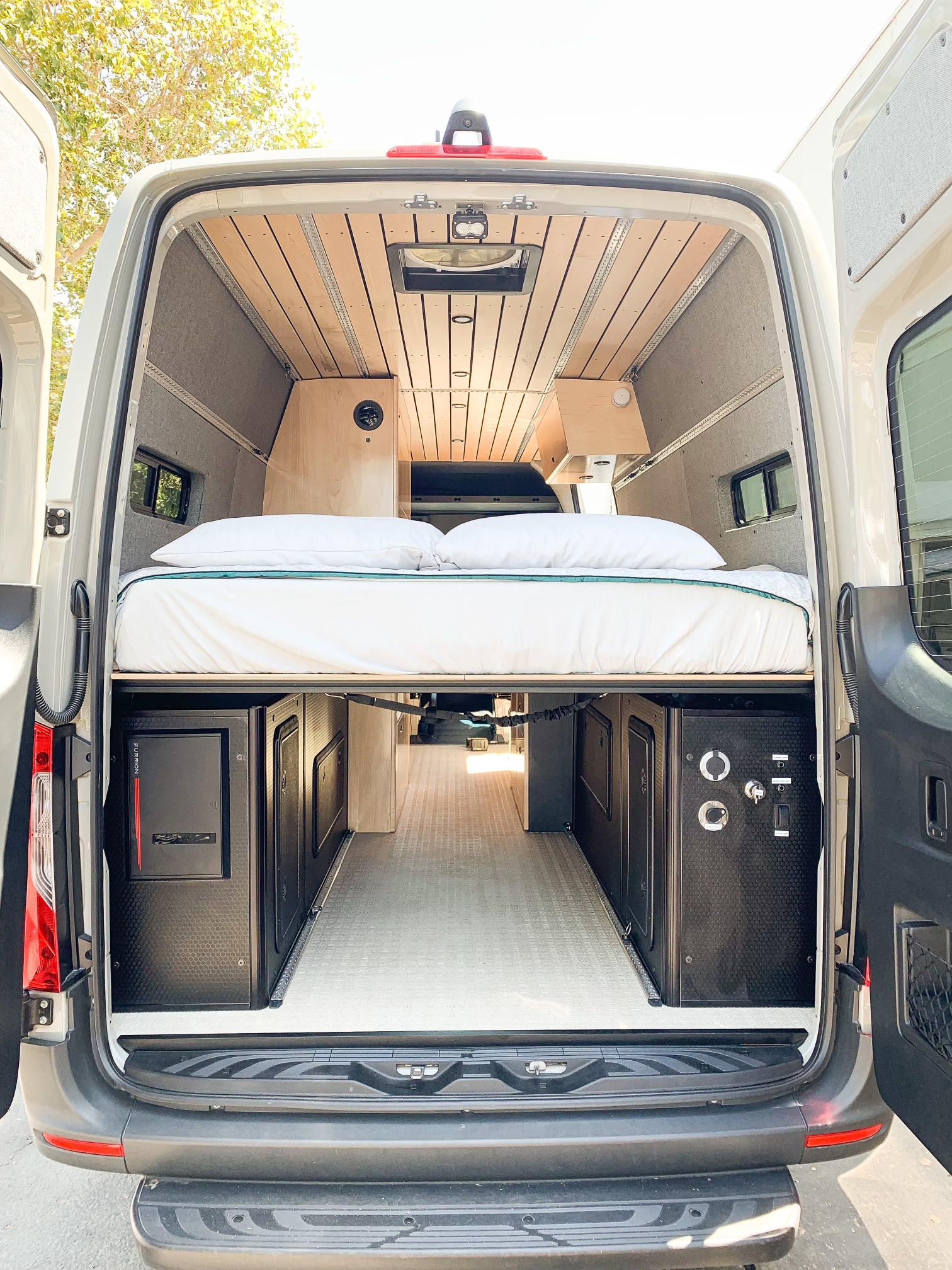 the back of a van with its doors open and a bed in the back .