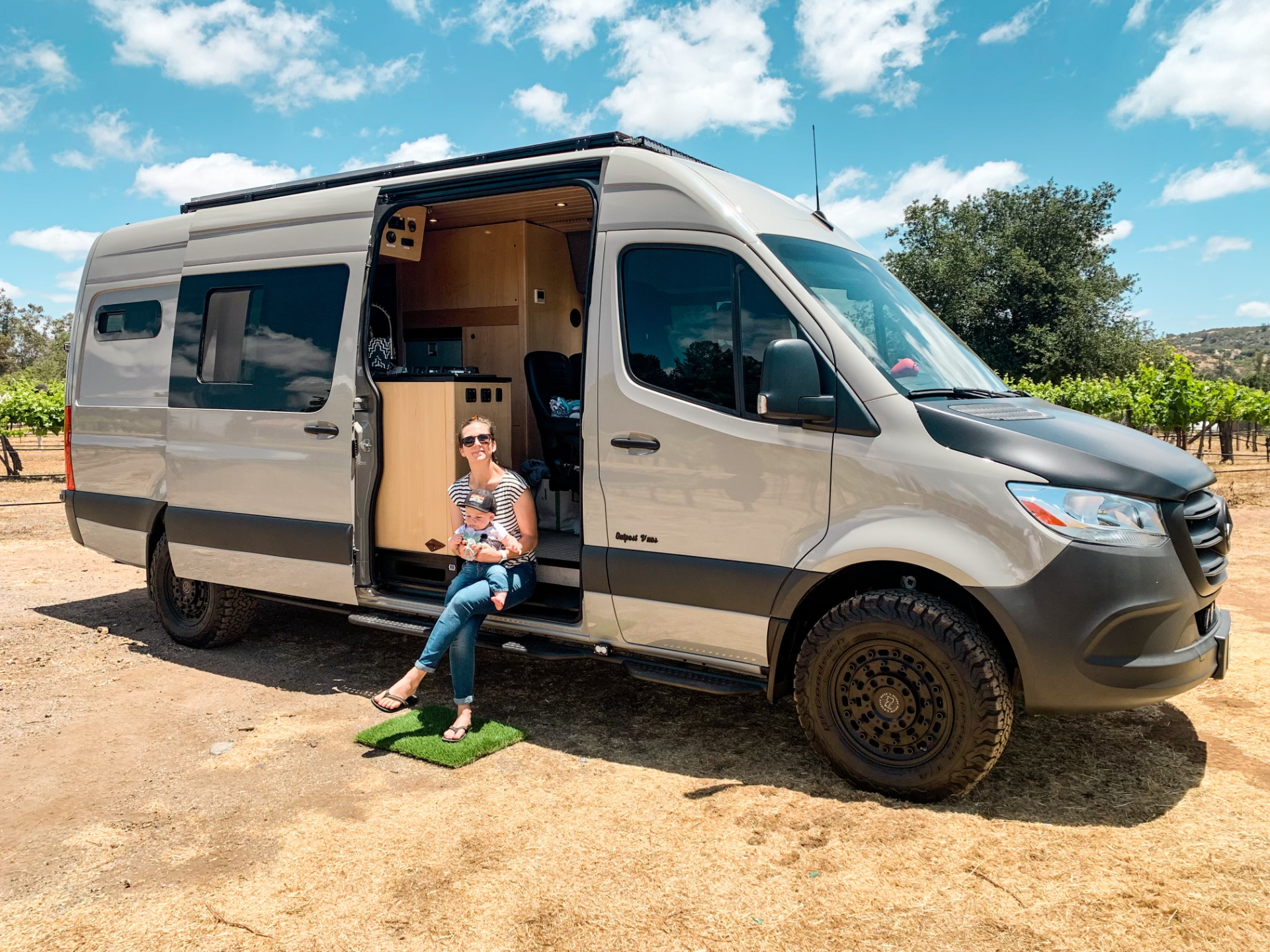 a woman is sitting on the steps of a van holding a baby .