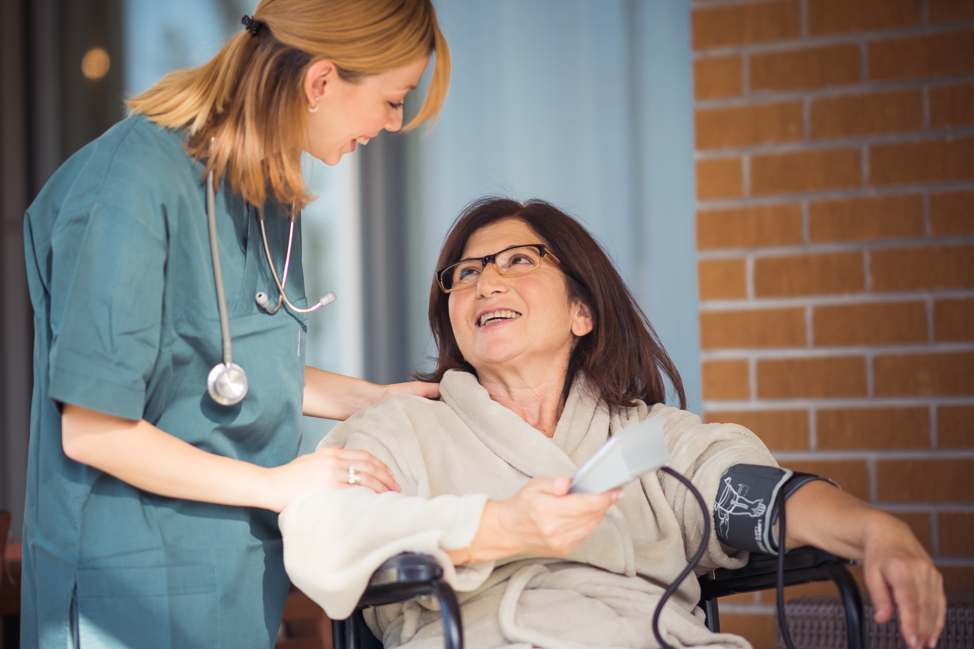 Nurse talking with a smiling patient in a wheelchair beside a brick wall