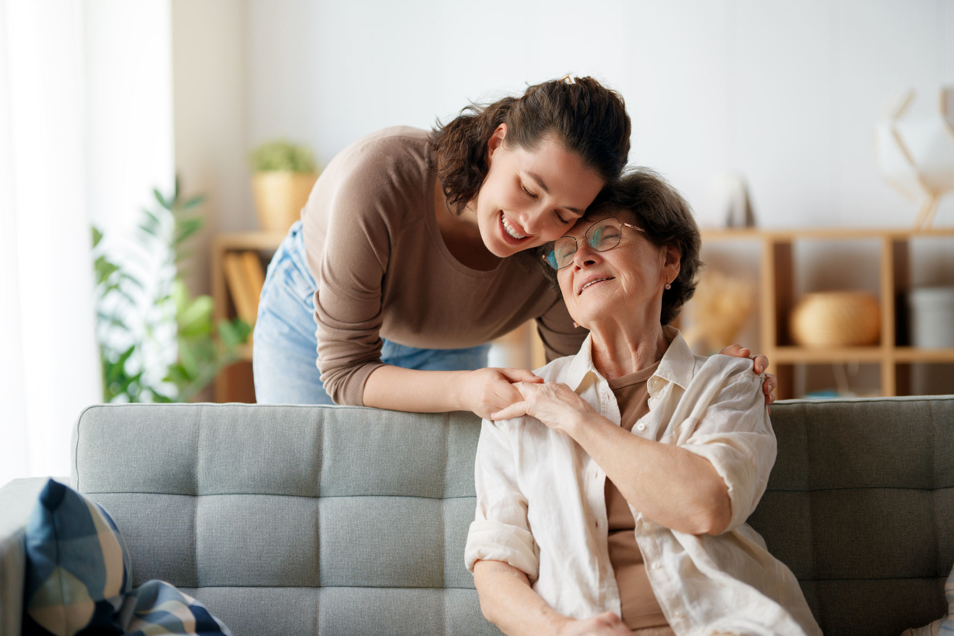 Two people smiling and embracing on a gray sofa in a bright living room
