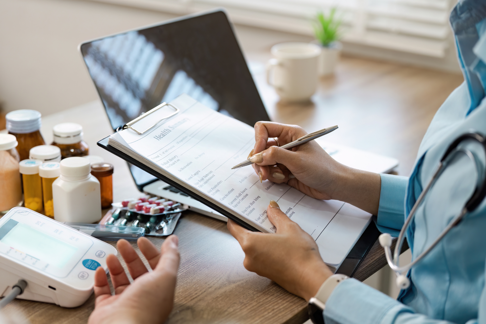 Medical professional writing on a clipboard beside pill bottles and a blood pressure monitor on a desk