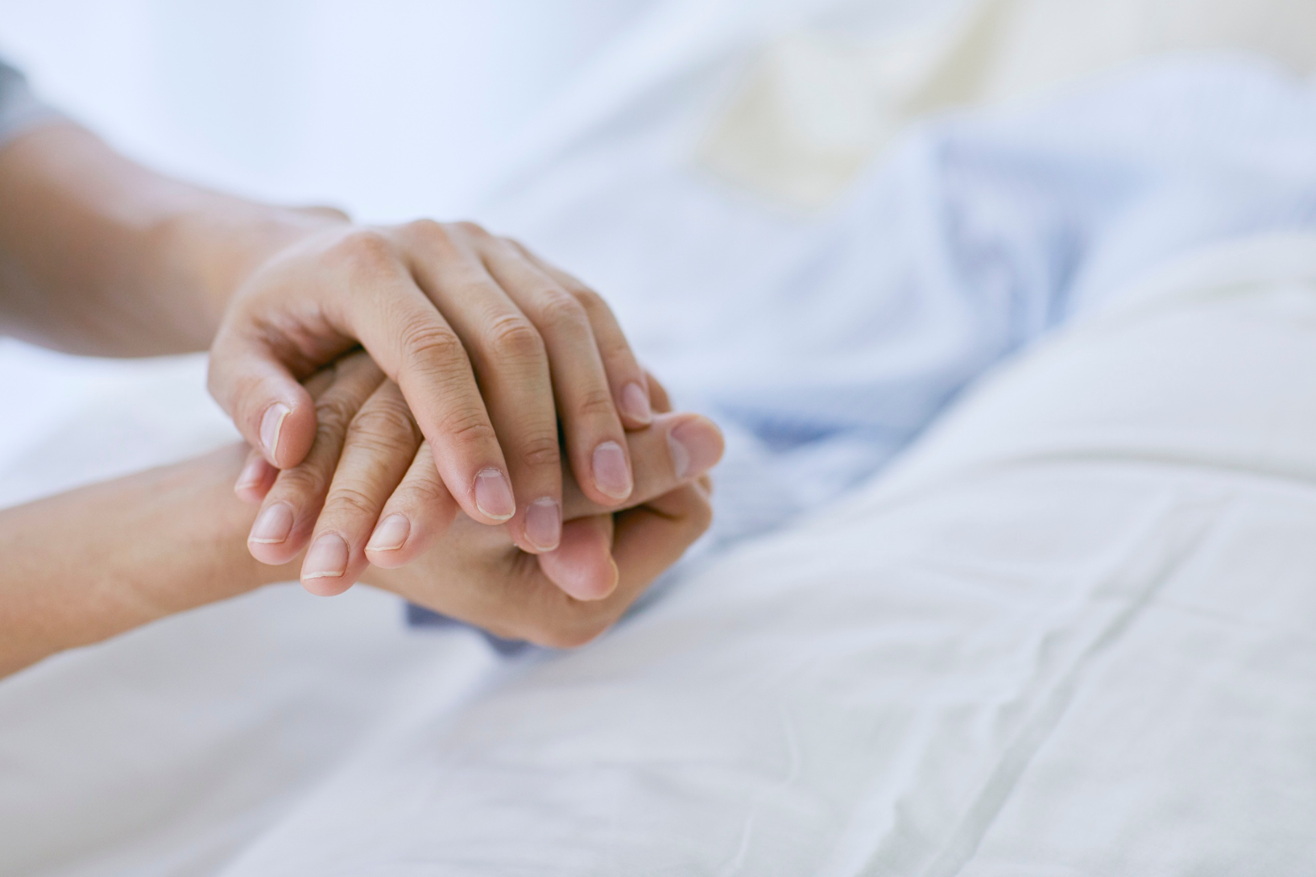 Hands clasped on a white hospital bed, suggesting comfort or support