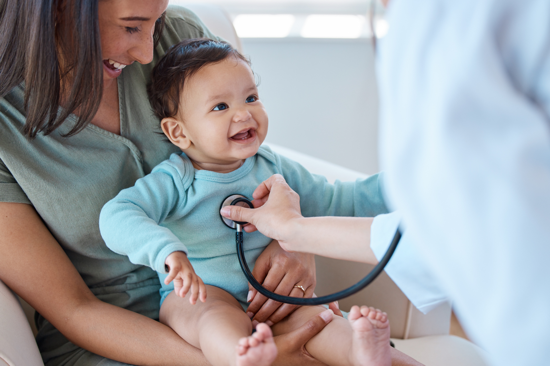 Adult checking a smiling baby’s heartbeat with a stethoscope in a bright clinic