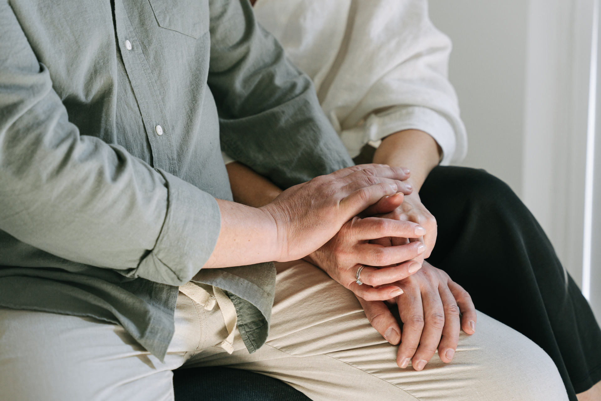 Two people sitting close together, holding hands in a quiet, soft-lit setting