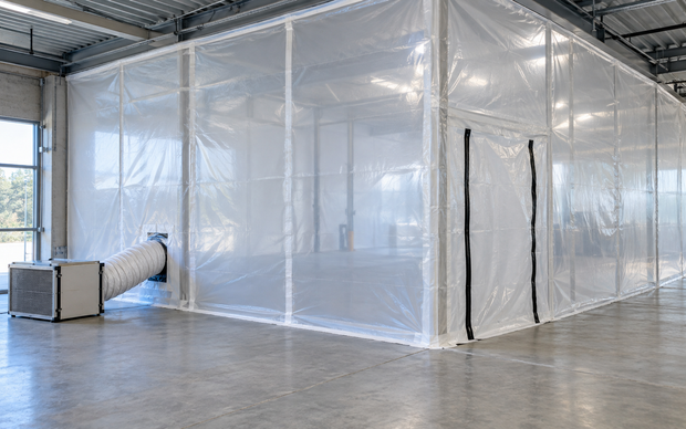 Large white plastic-enclosed room in an industrial warehouse, with a duct and floor vent.