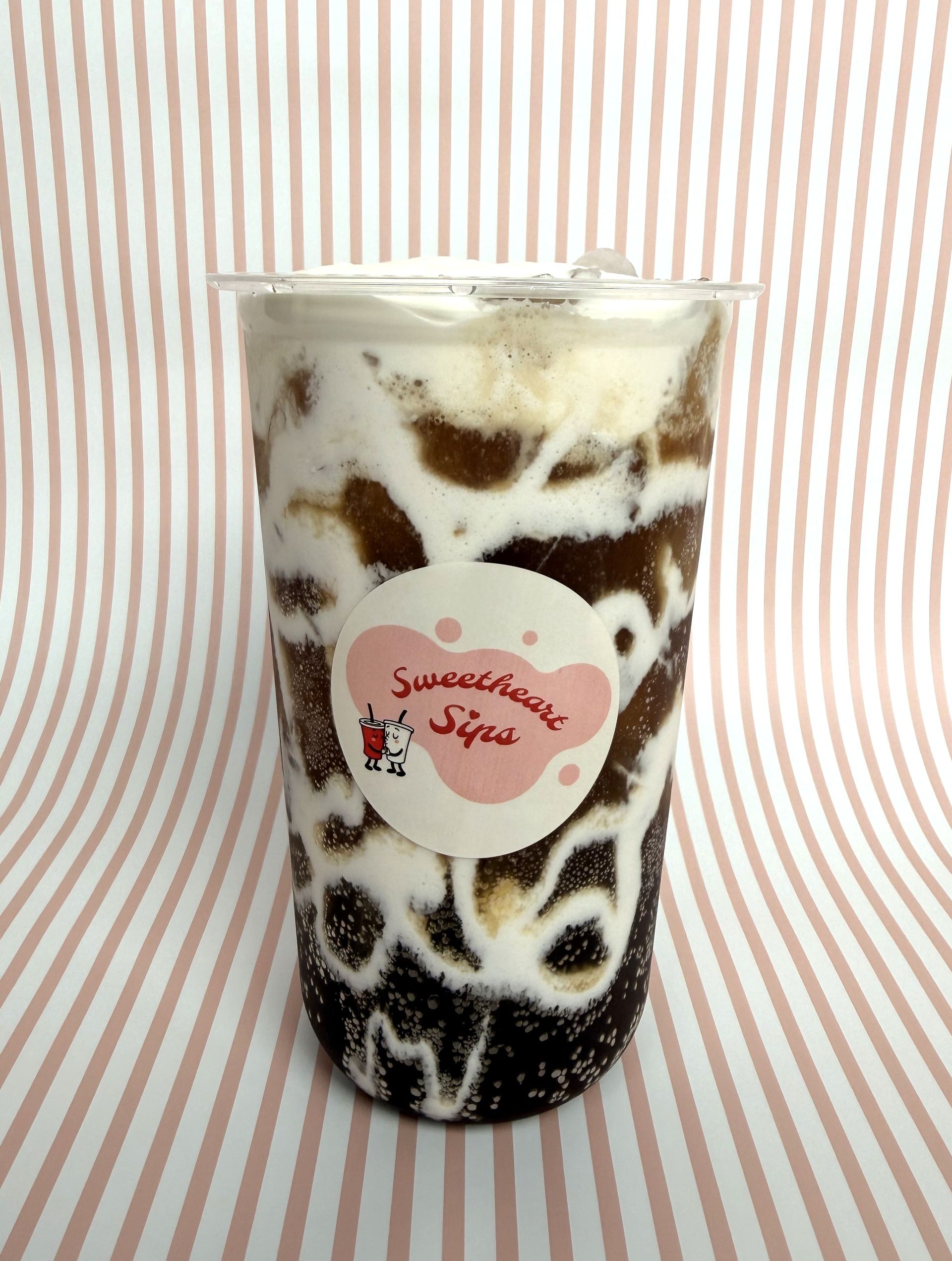 Our drink called the Heathcliff in our Sweetheart Sips branded cup against a pink and white striped background.