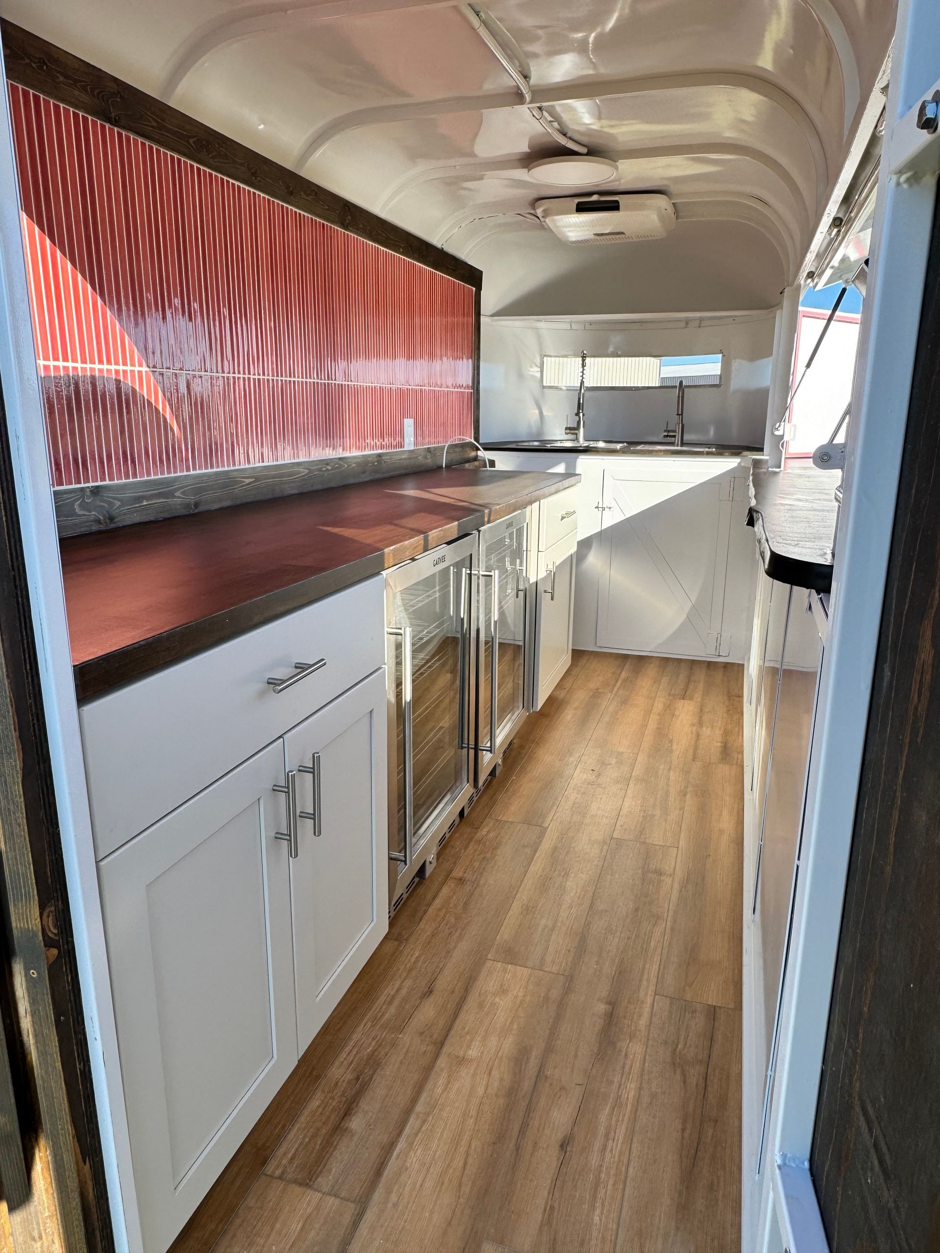 Interior of a converted horse trailer with white cabinets, wood countertops, and red patterned wall panels
