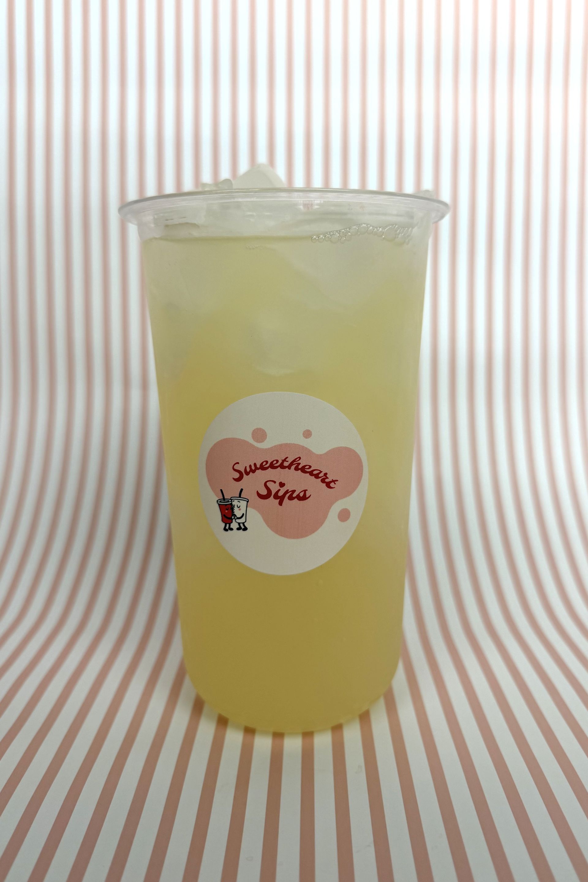 Lemonade in our Sweetheart Sips branded cup against a pink and white striped background.