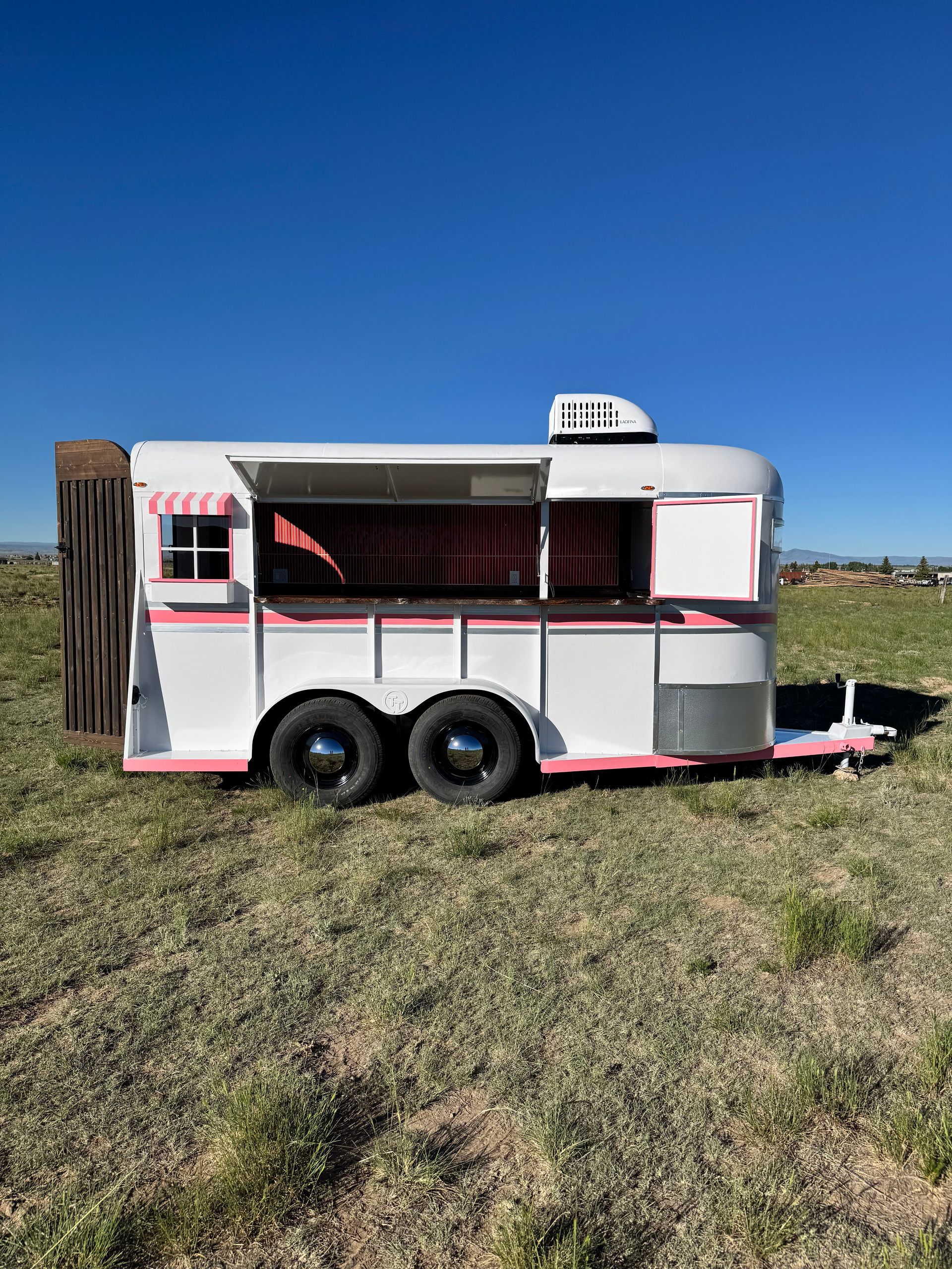 Pink-and-white horse trailer parked on grass under a clear blue sky