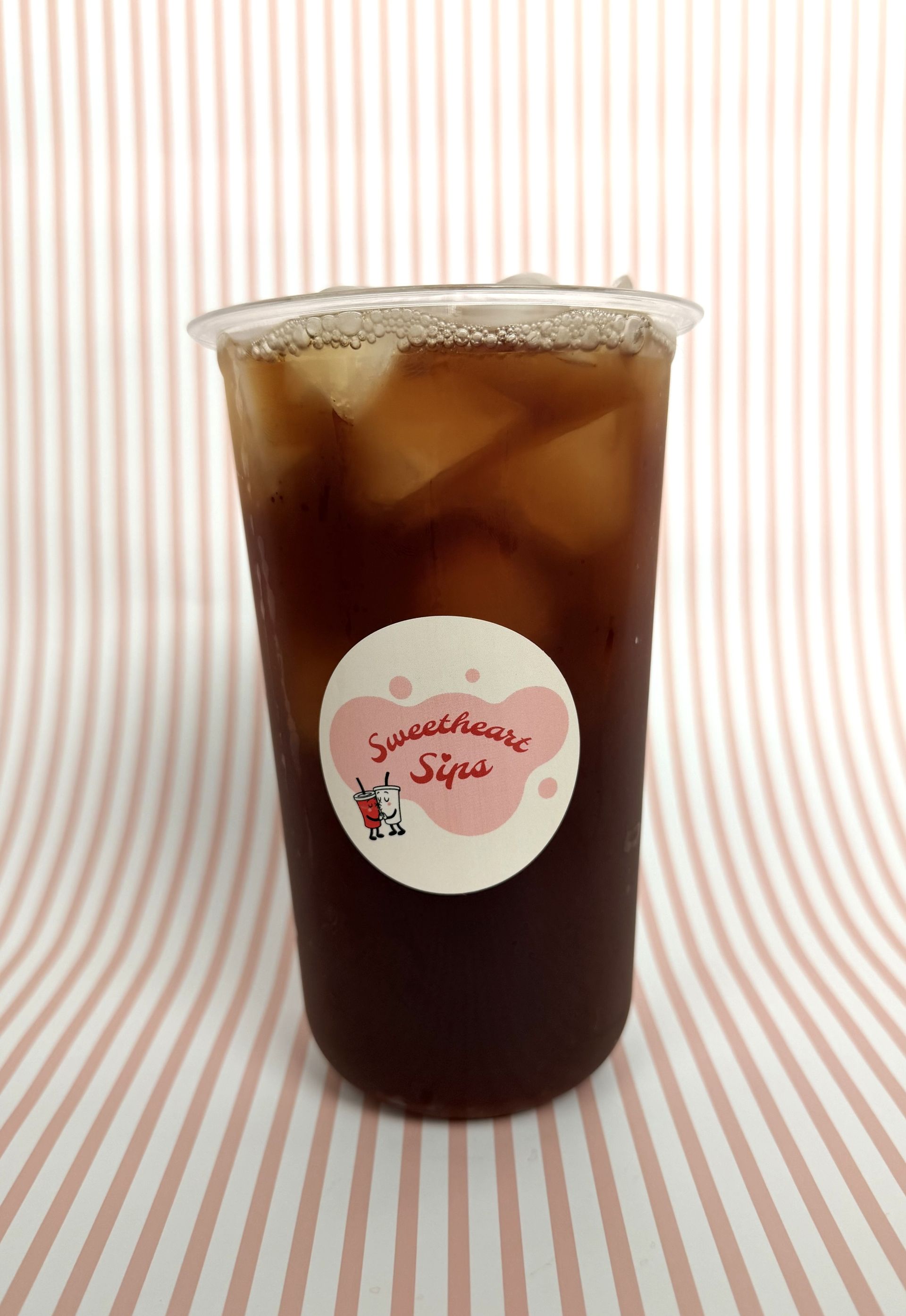 Iced tea in our Sweetheart Sips branded cup against a pink and white striped background.