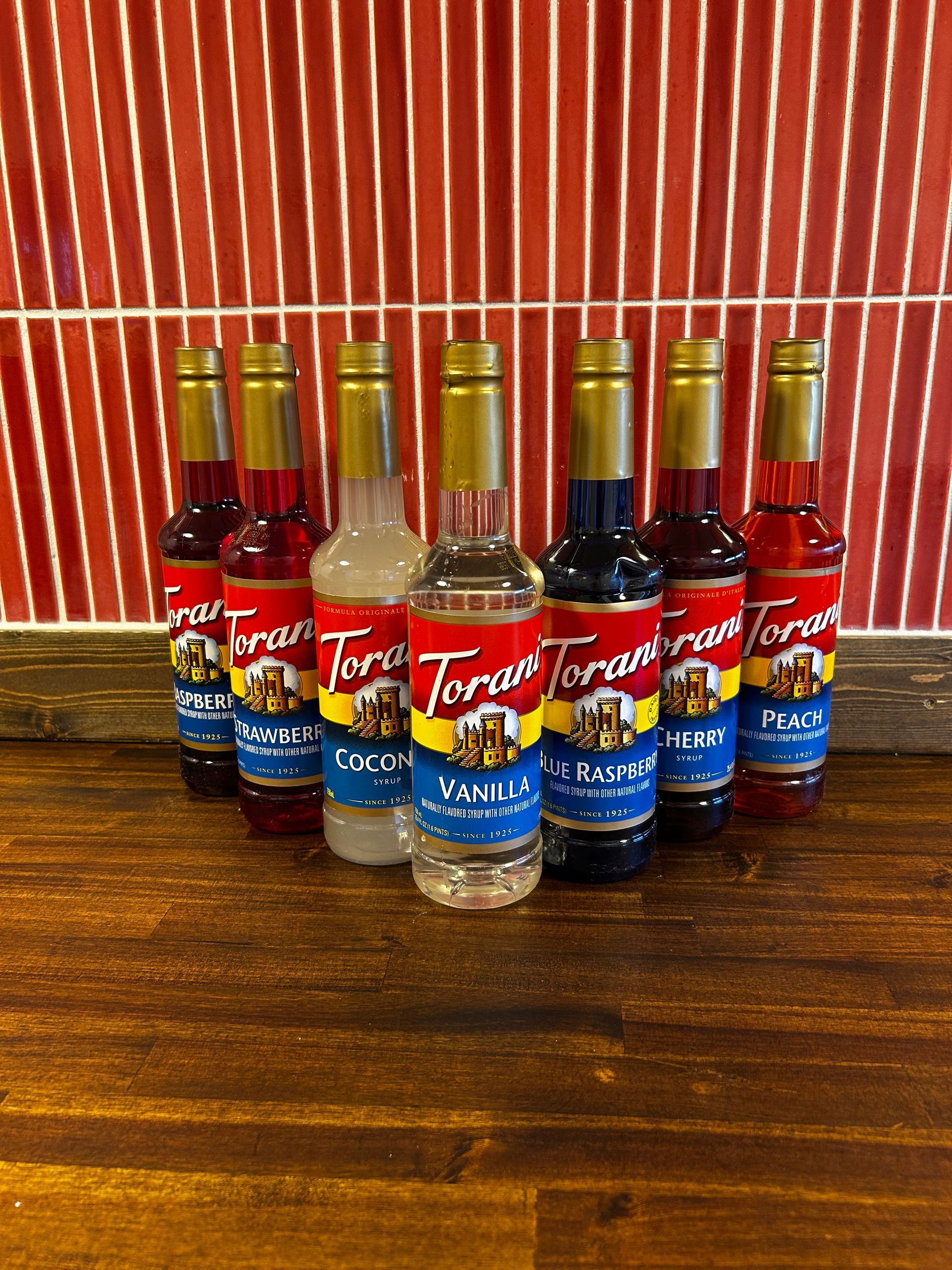 Five Torani syrup bottles in assorted flavors on a wooden shelf