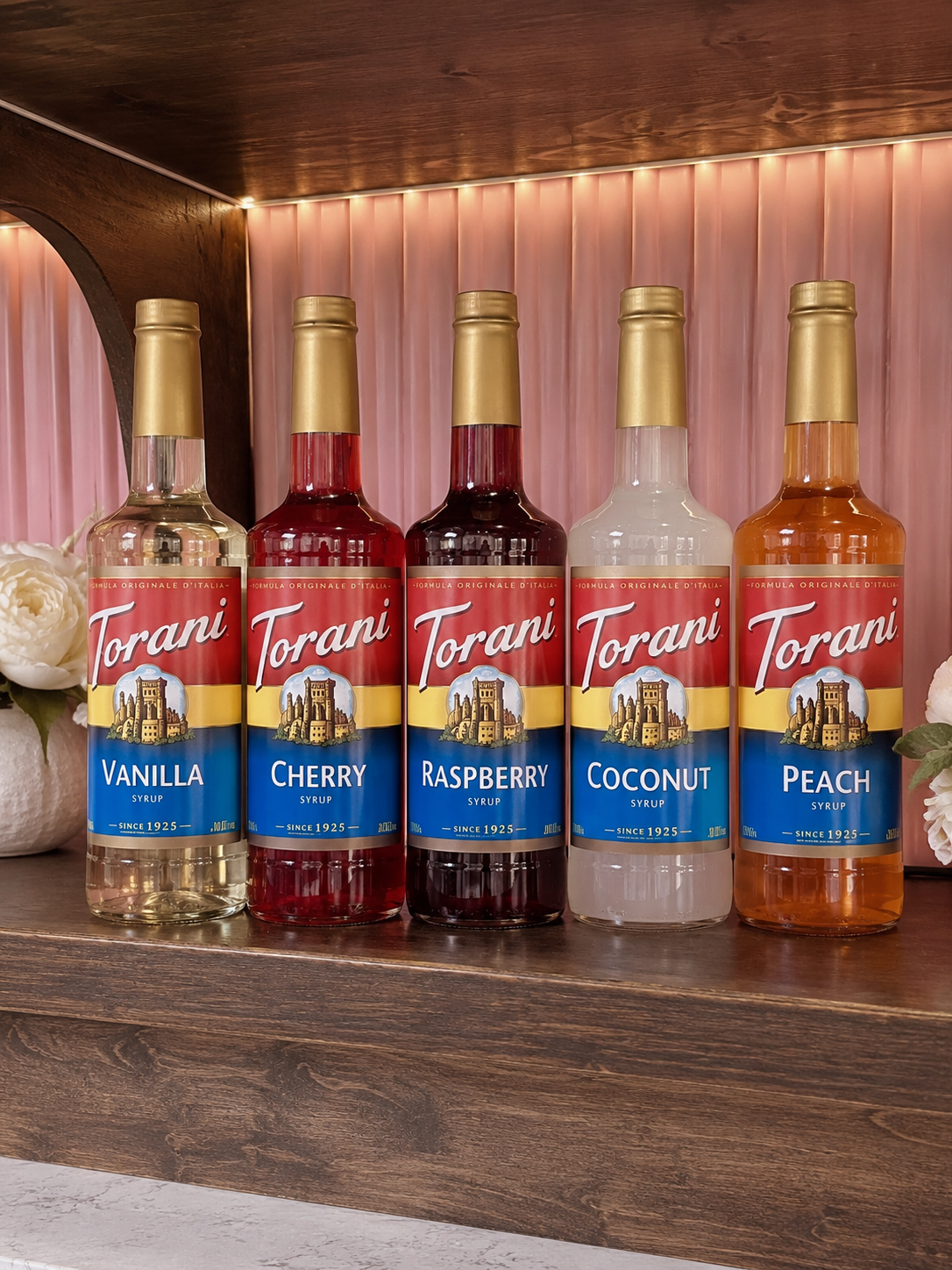 Five Torani syrup bottles in assorted flavors on a wooden shelf