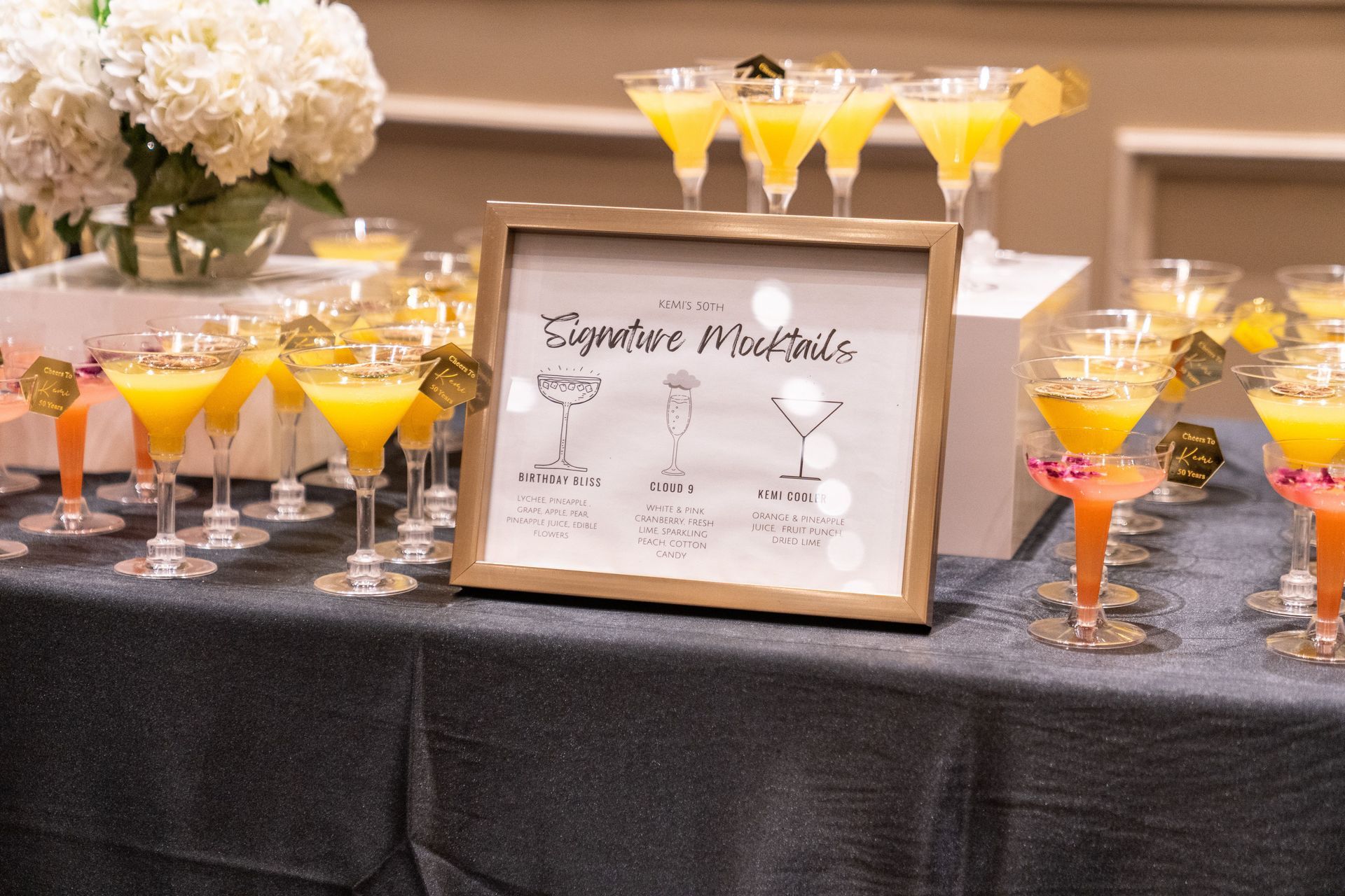 Cocktail display on black table with framed sign and martini glasses of orange-yellow drinks at a wedding reception