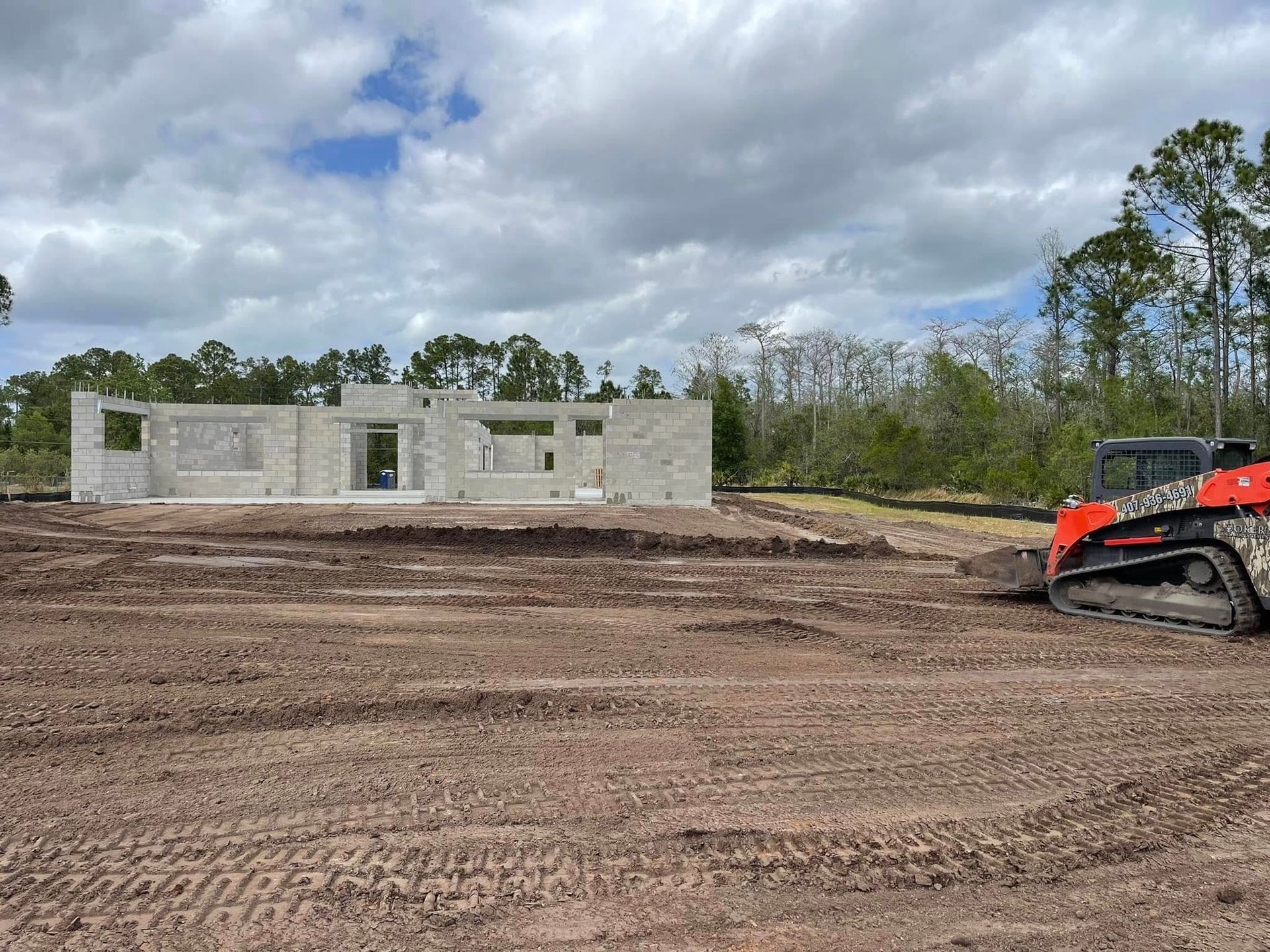 Construction site with unfinished concrete building and orange excavator under cloudy sky