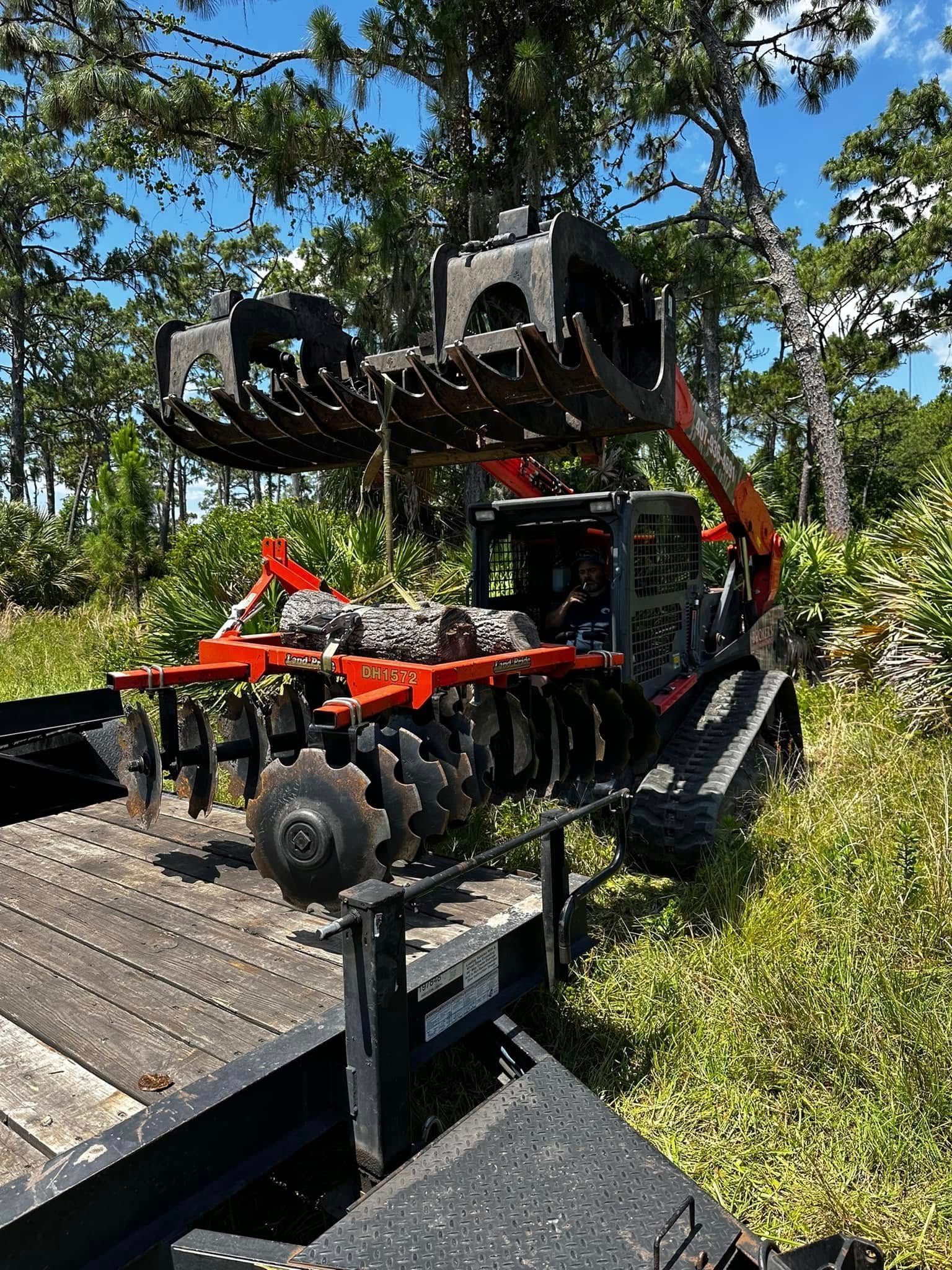 Red and black tractor with brush cutter attachment on a wooded hillside near a wooden ramp.