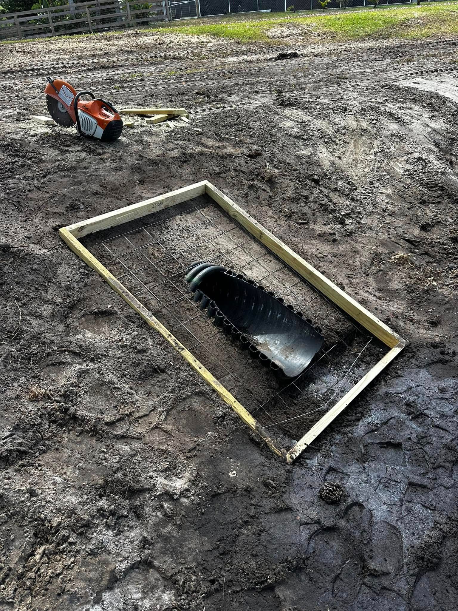 Mud-covered excavation site with a rectangular opening bordered in wood and an orange tool nearby.