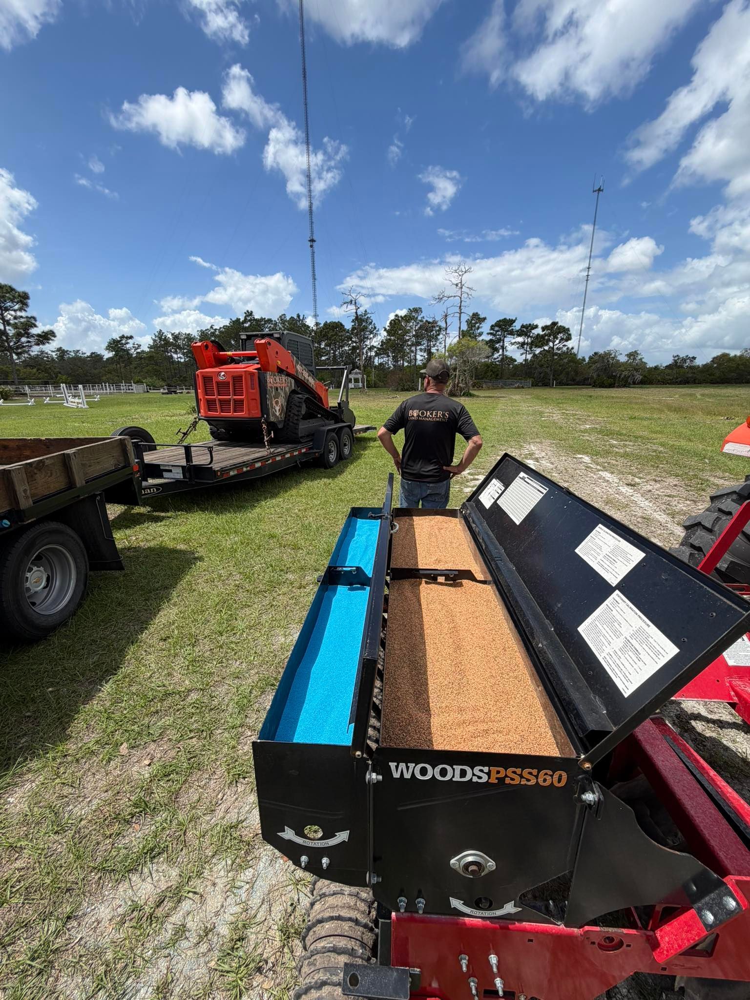 Man standing beside open Woodizer log splitter with blue and brown wood chips in a grassy field under a cloudy sky