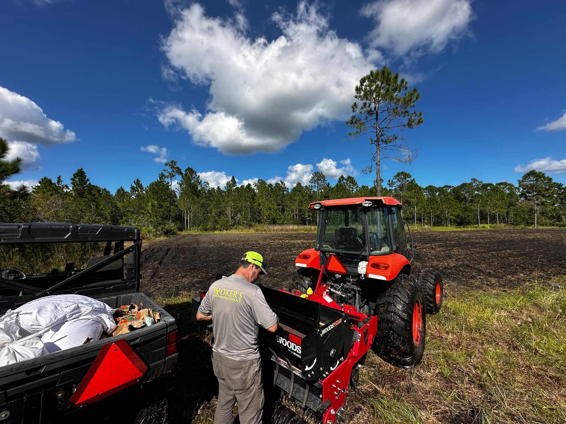 Person loading equipment onto a red tractor in a field under a blue sky.