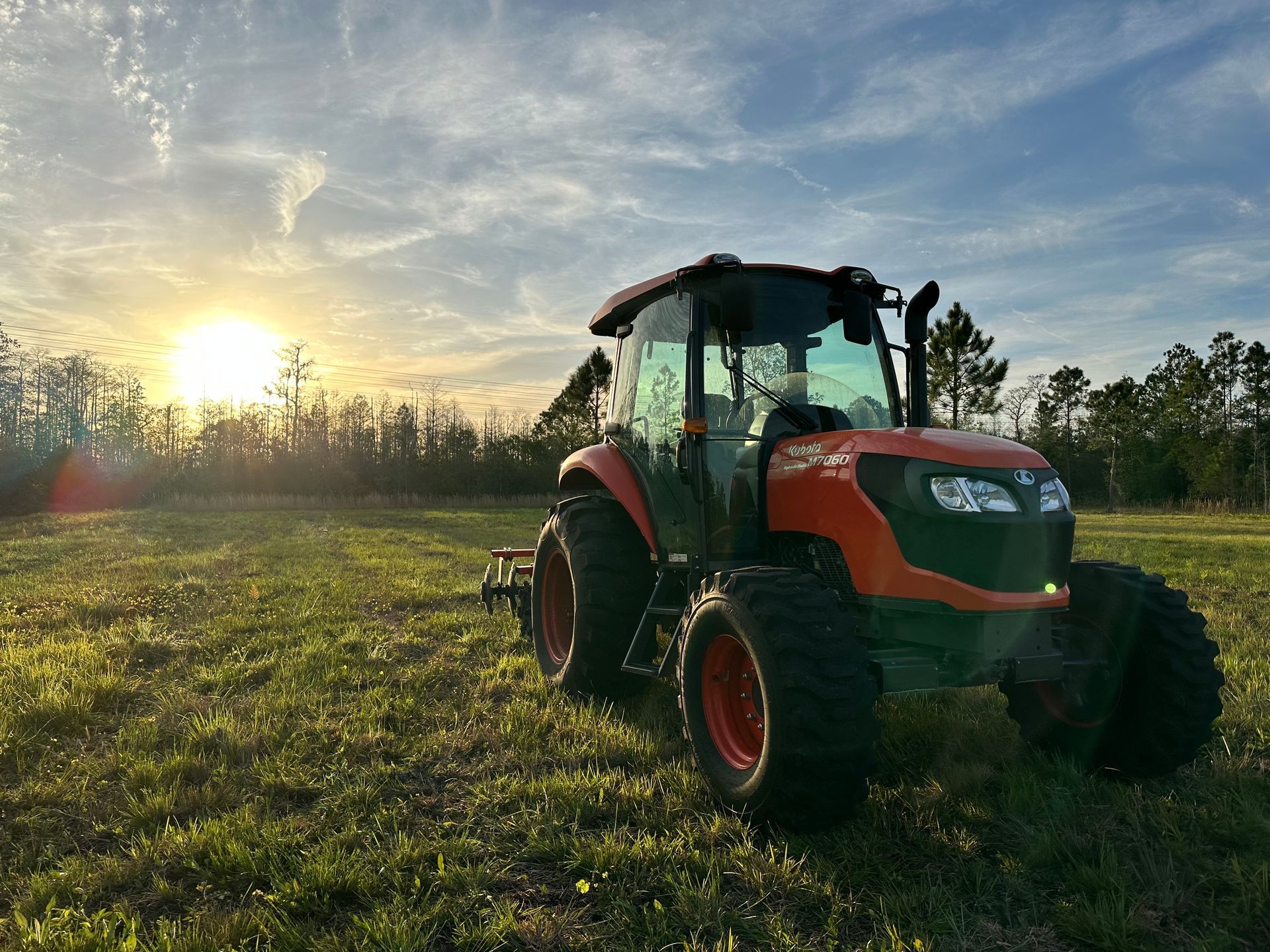 Orange tractor in a field at sunset with trees in the background