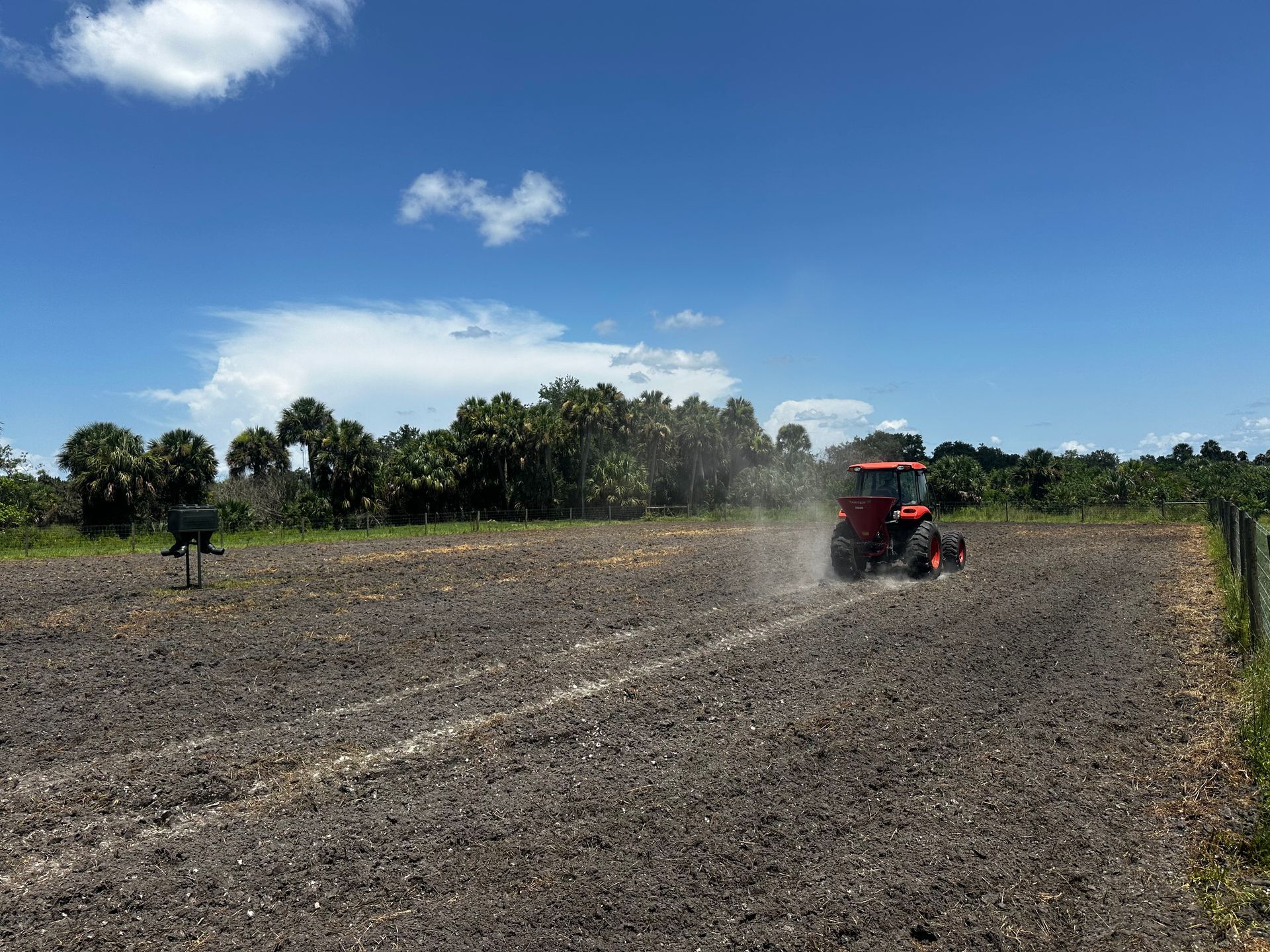 Red tractor spraying dust across a plowed field under a blue sky