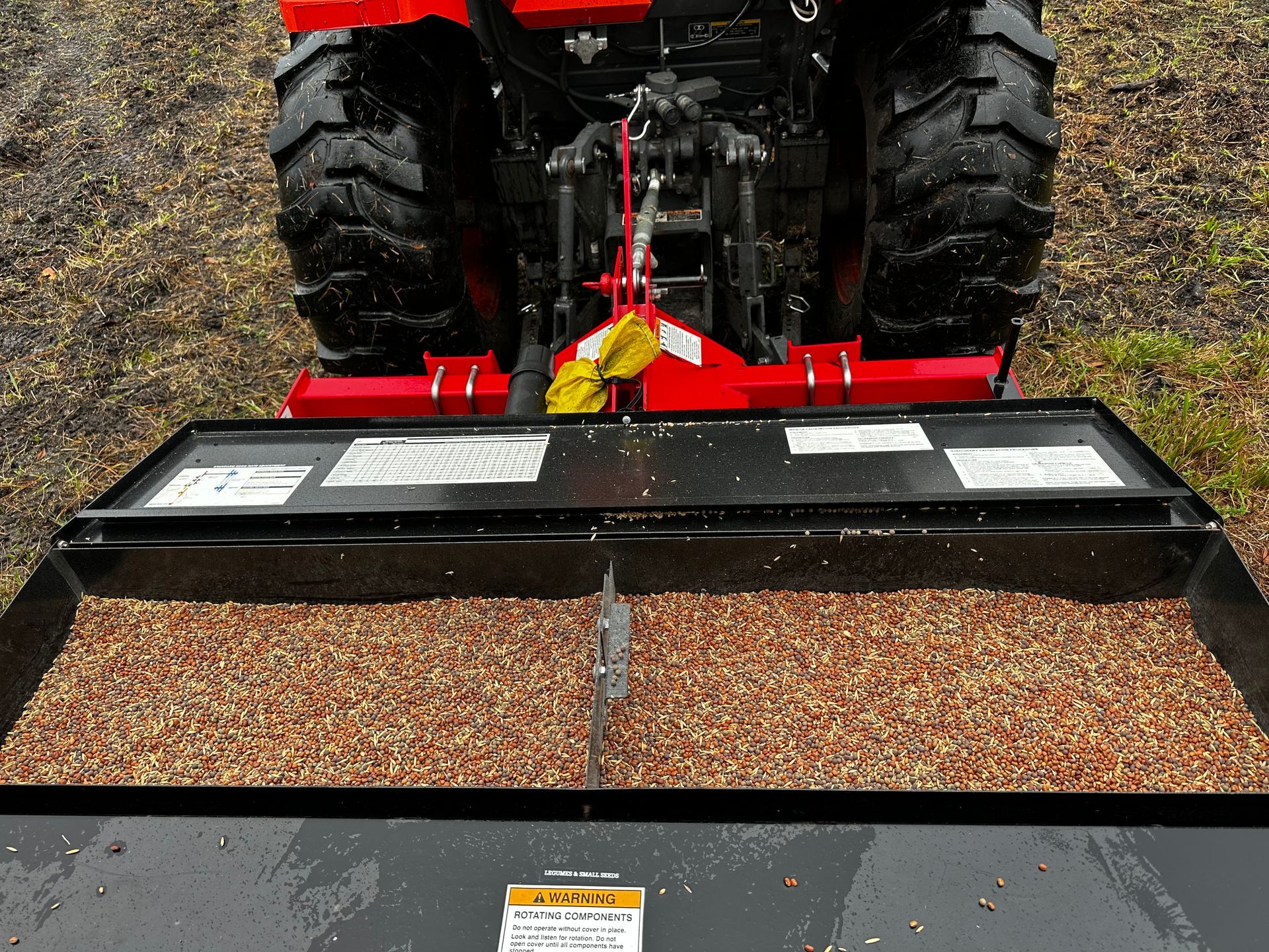 Rear view of a red tractor spreading gravel with a front-mounted black bucket outdoors