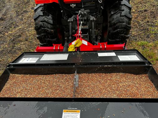 Red tractor pushing a black gravel bucket in a muddy field from a front-mounted view