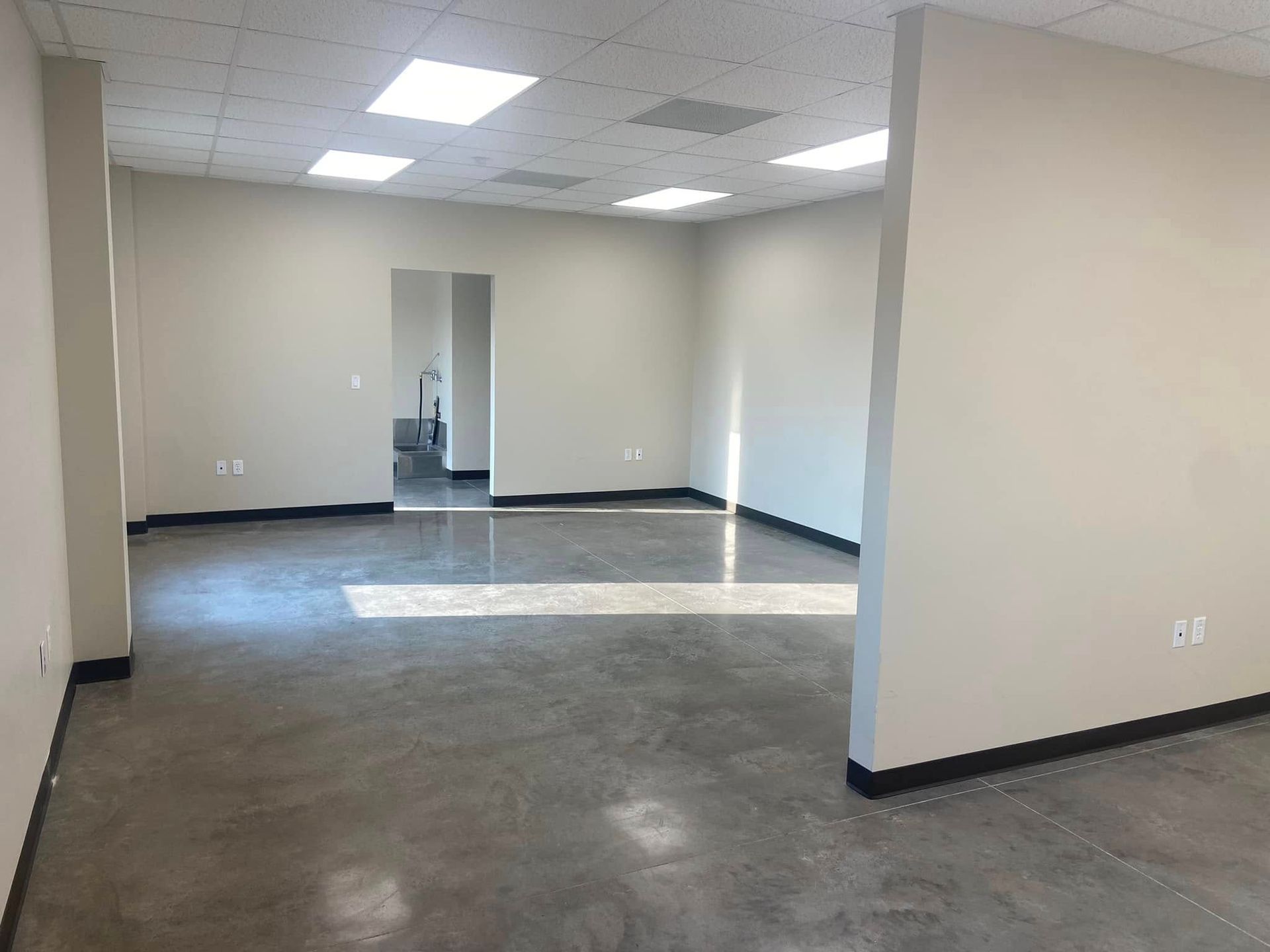 Empty office space with beige walls, gray floor, and bright fluorescent ceiling lights