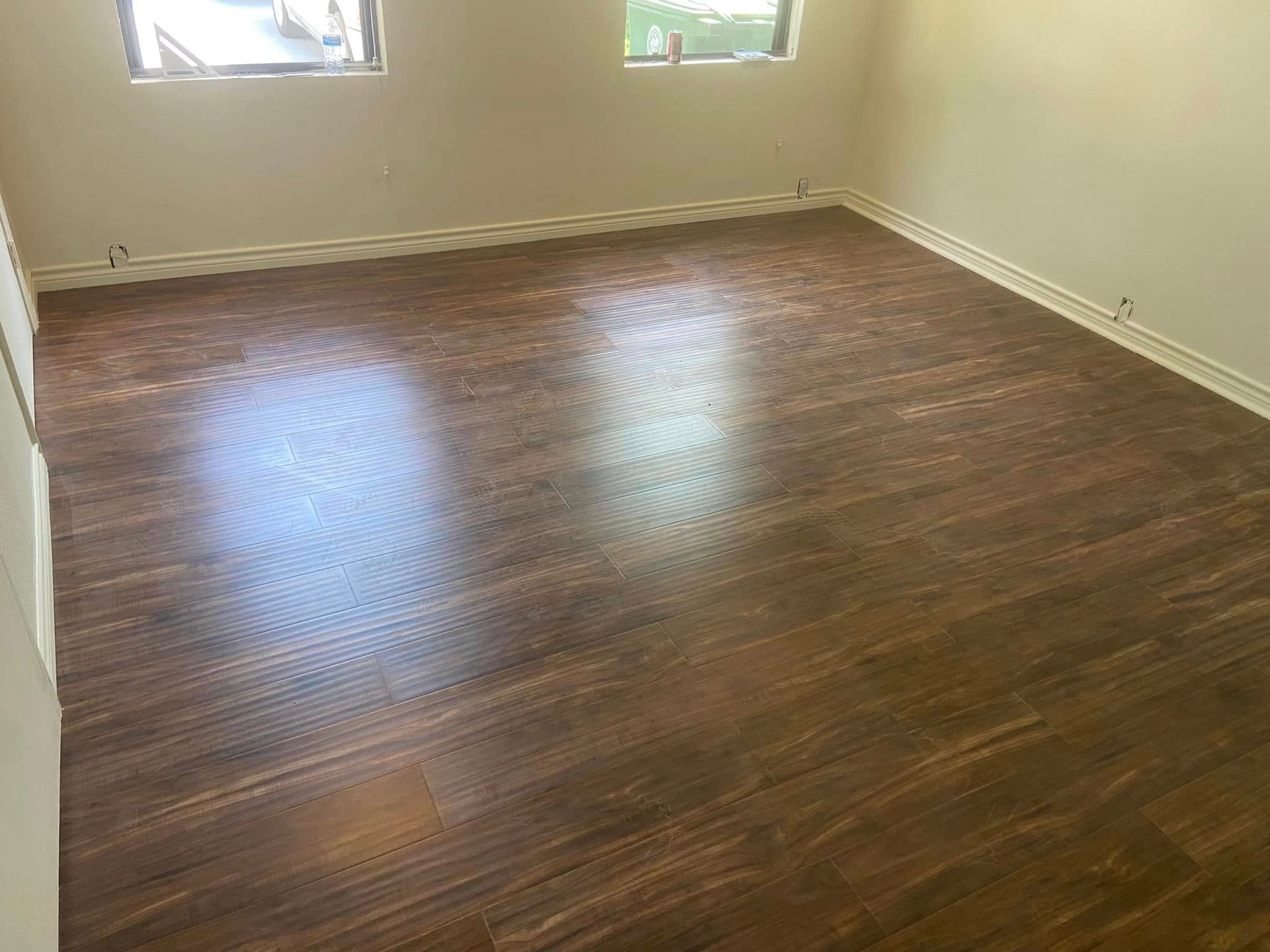 Empty room with brown wood flooring, beige walls, and a small window.