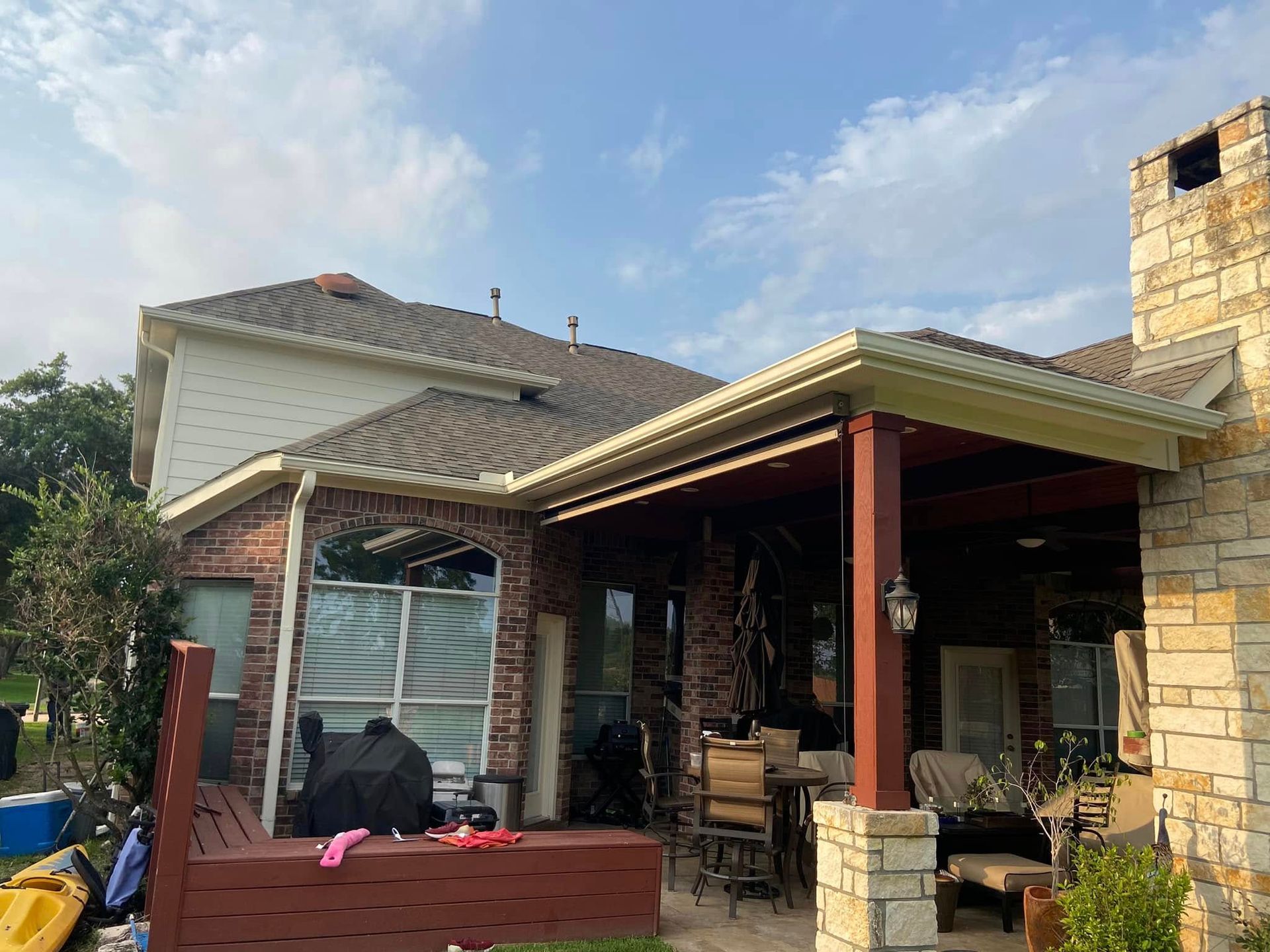 Backyard patio with brick seating, stone columns, and a covered porch beside a house