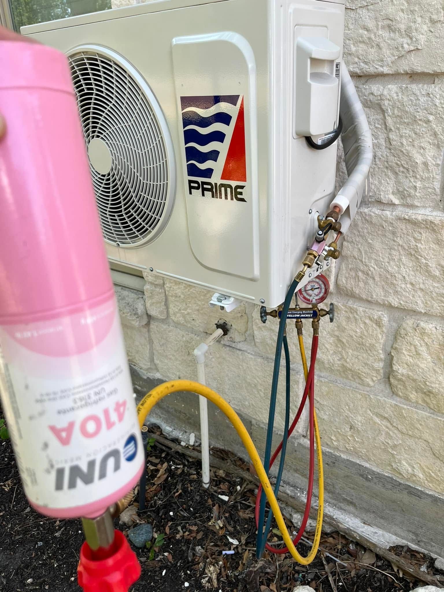 Outdoor heat pump unit with tangled colored cables beside a pink bottle in front of a wall