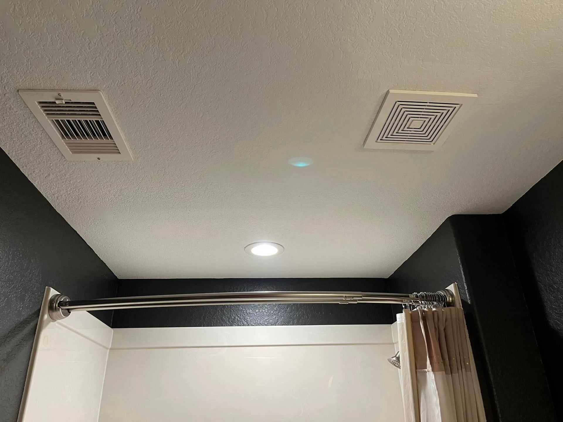Ceiling with two vents, two lights, and a shower curtain rod in a bathroom