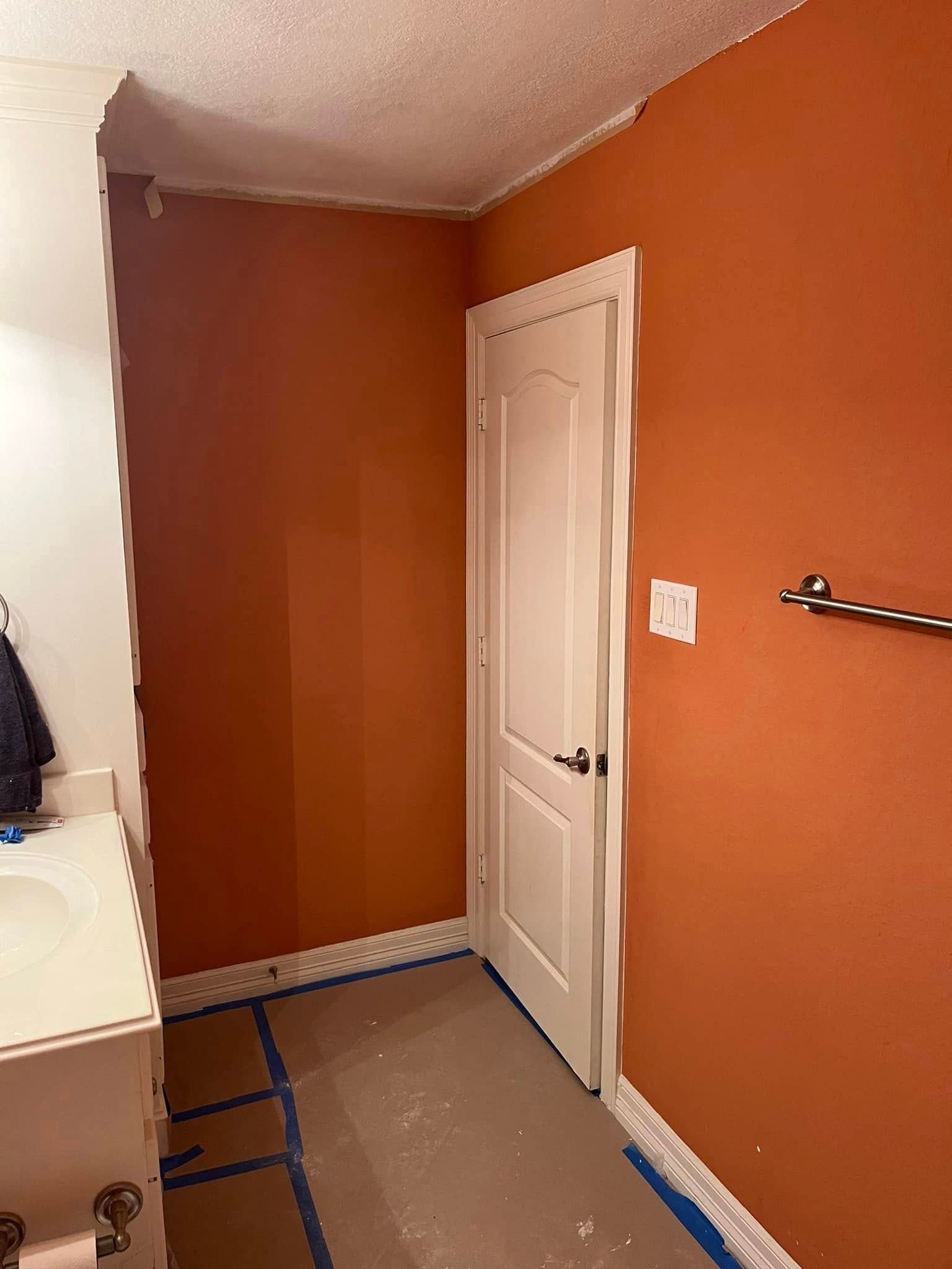 Small bathroom with orange walls, white door, towel rack, and a vanity under renovation.