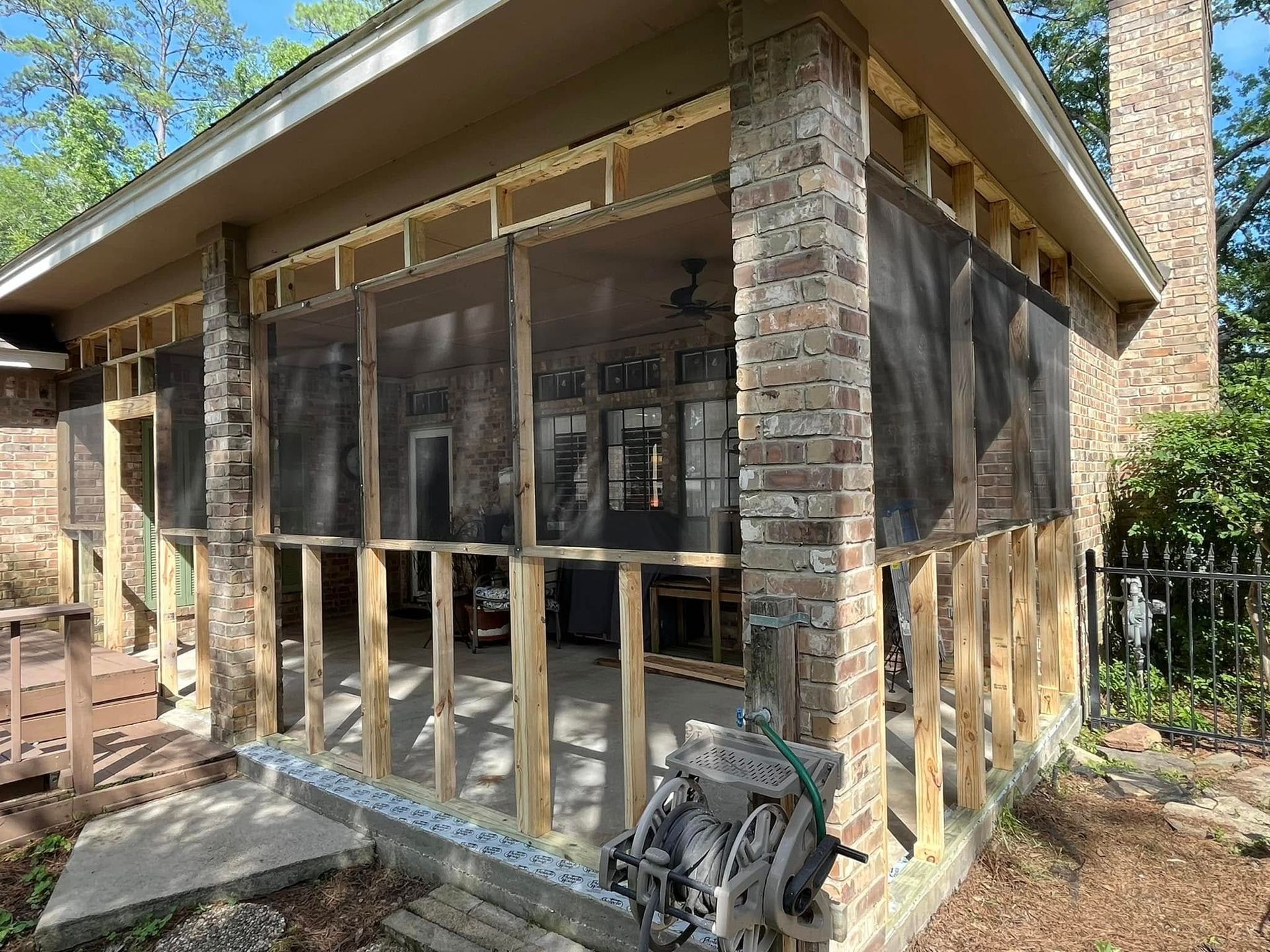 Partially enclosed porch under construction with exposed wooden framing and mesh screening