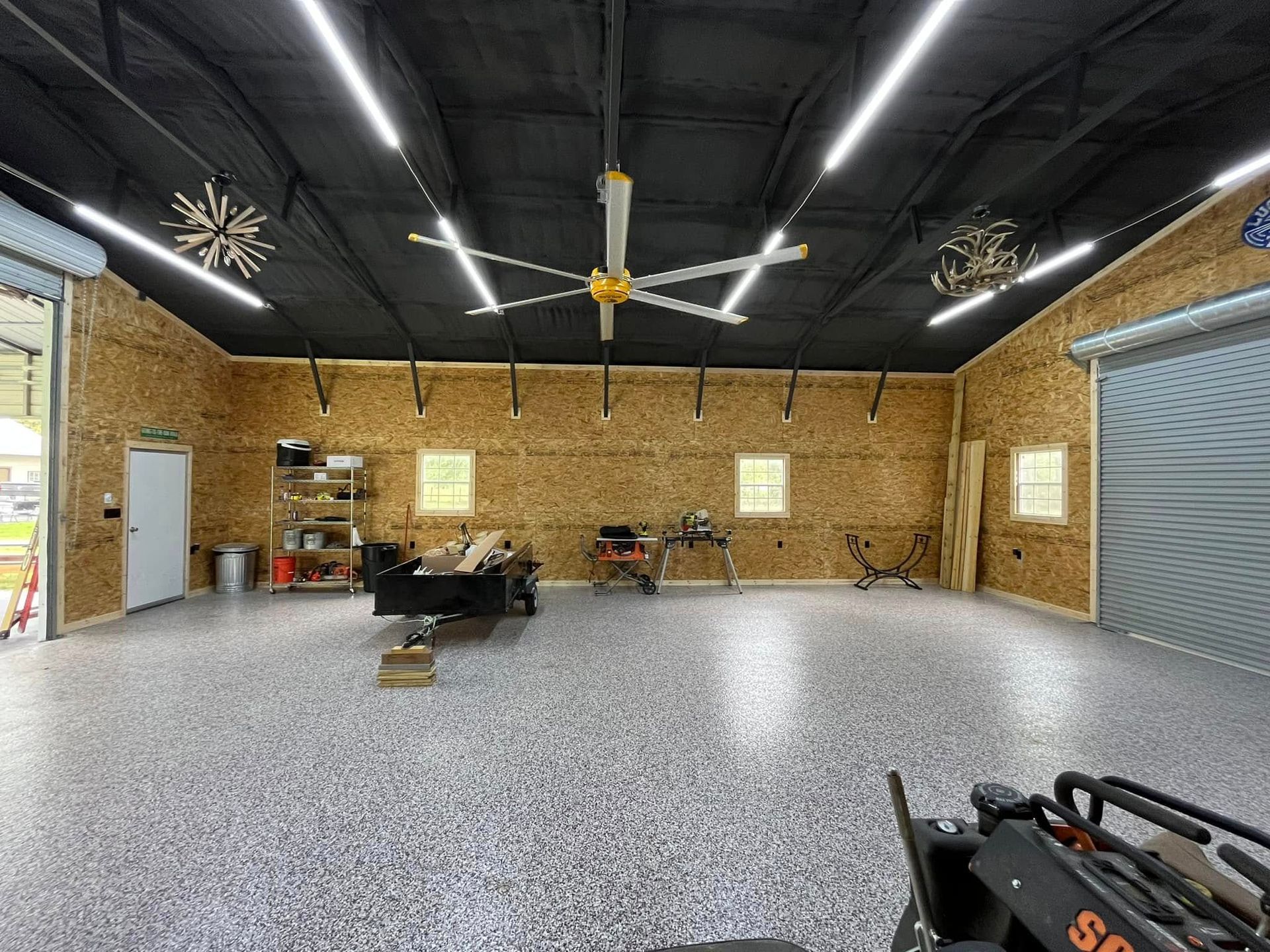 Large indoor workshop with concrete floor, wood walls, ceiling fans, and tools along the sides