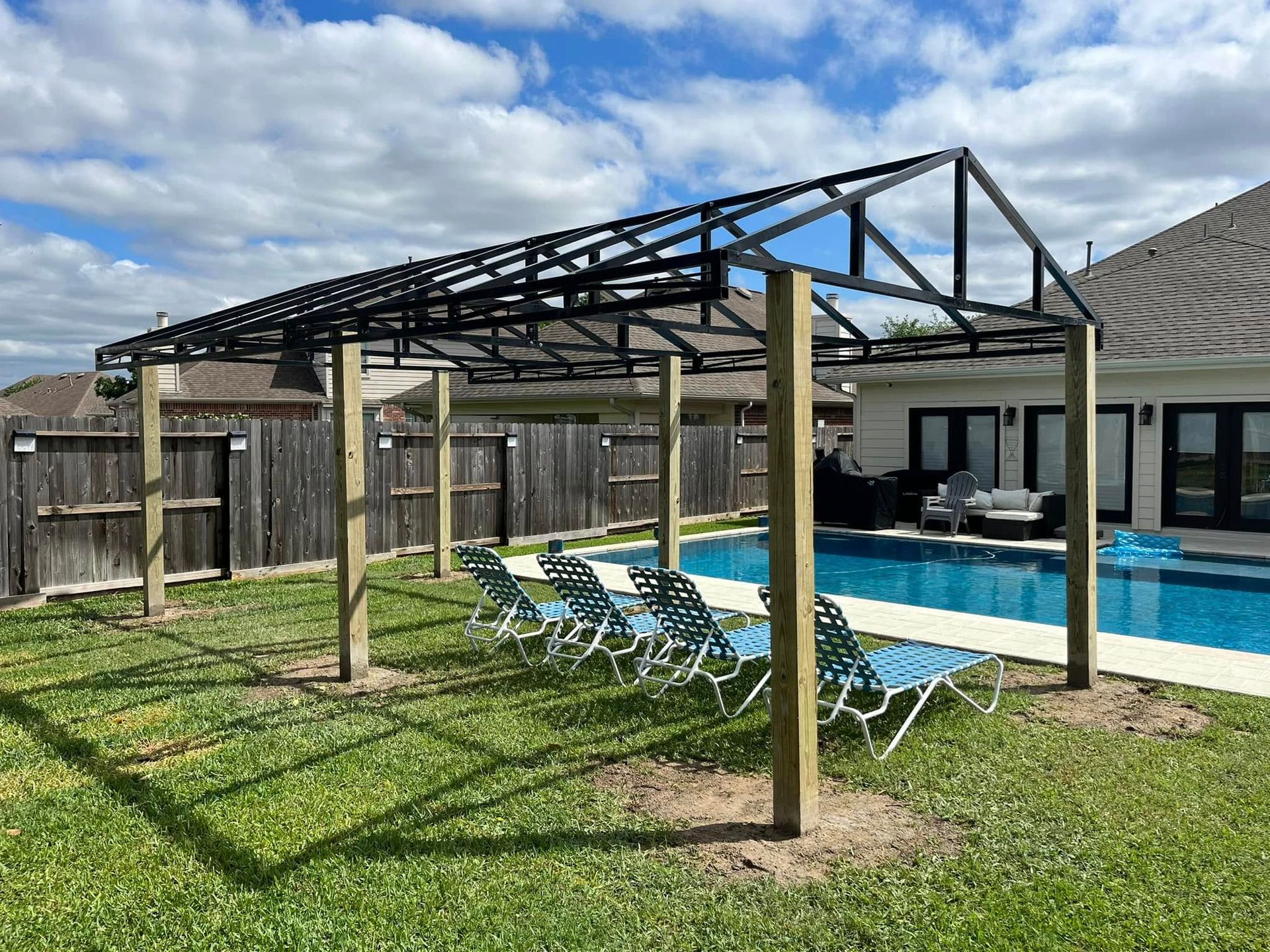 Backyard pool area with a wooden pergola frame and several turquoise lounge chairs under a blue sky