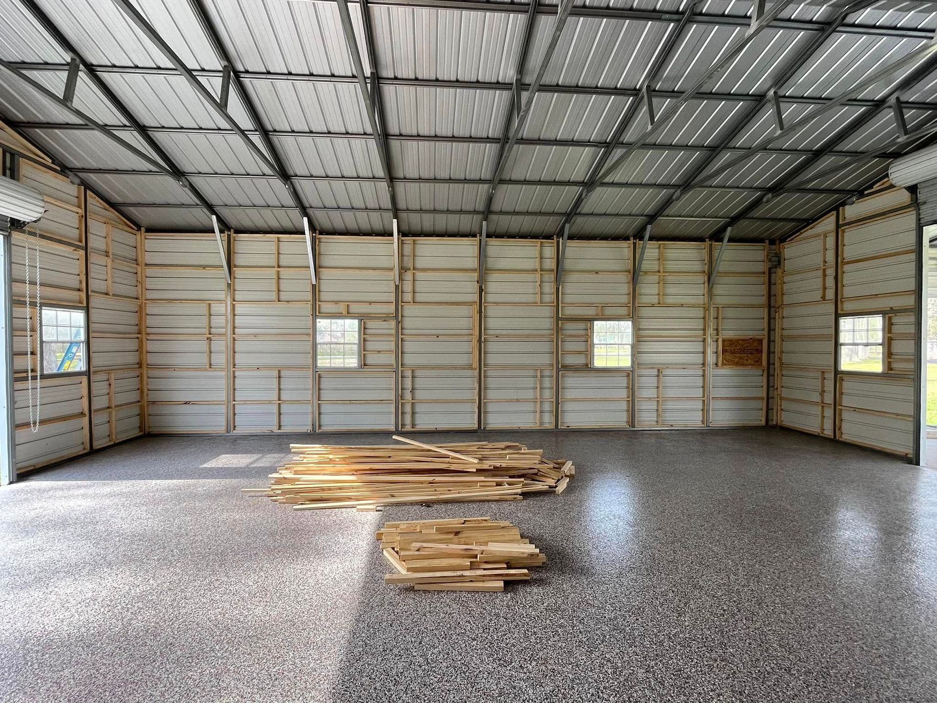 Empty metal-framed warehouse interior with stacked wooden boards on a concrete floor