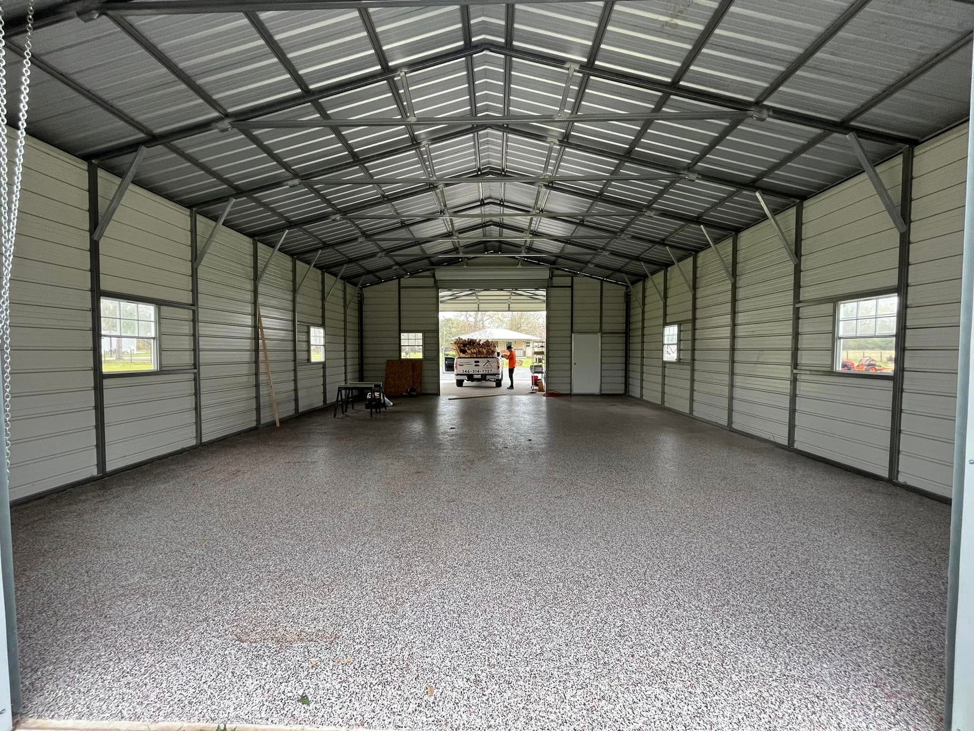 Empty metal storage shed with a speckled floor and open doorway at the far end